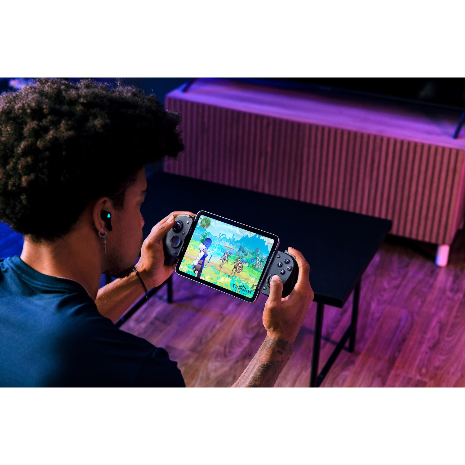A person is holding a tablet with game controllers attached. They are playing a game. The background has a table and a cabinet.