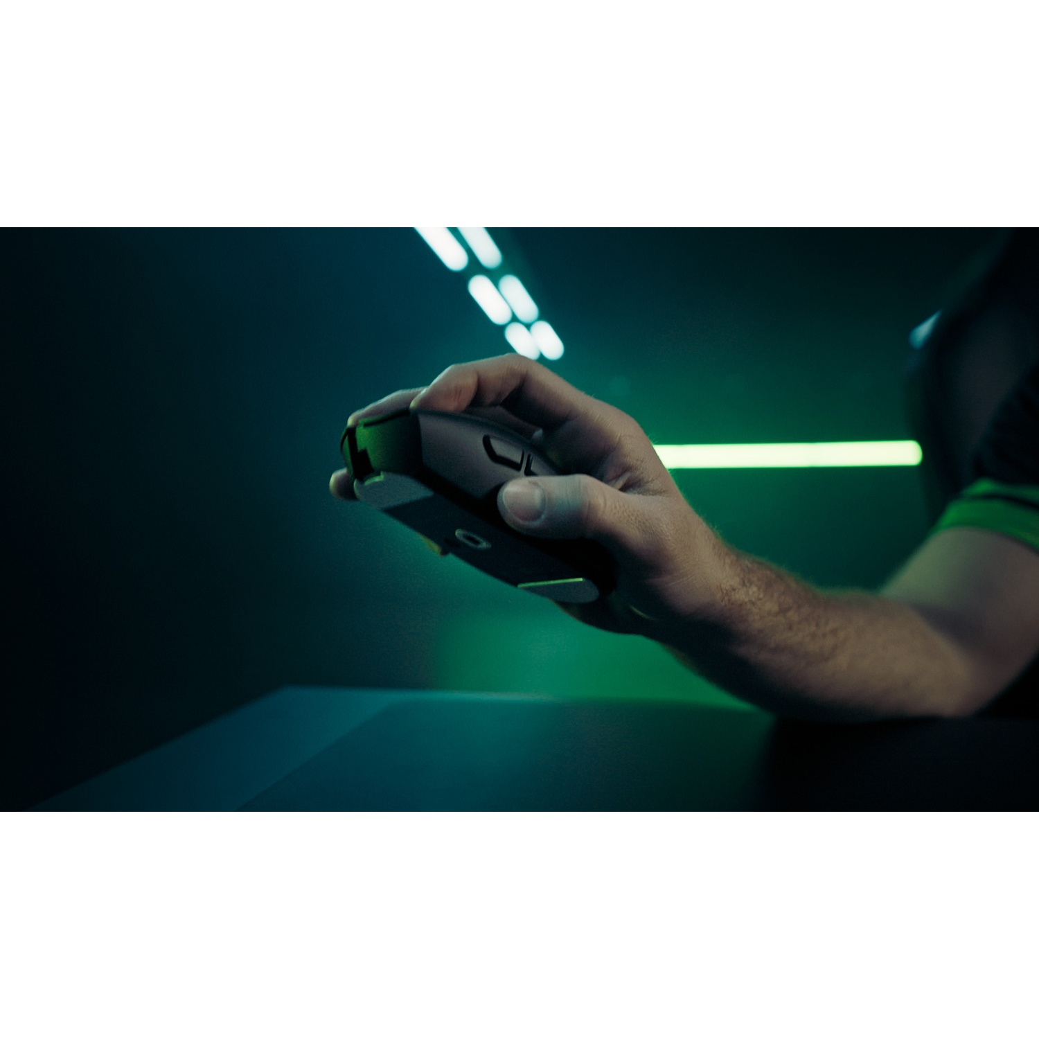 Une main tenant une souris de jeu noire. Le fond présente des lumières vertes et blanches et un environnement sombre et flou.