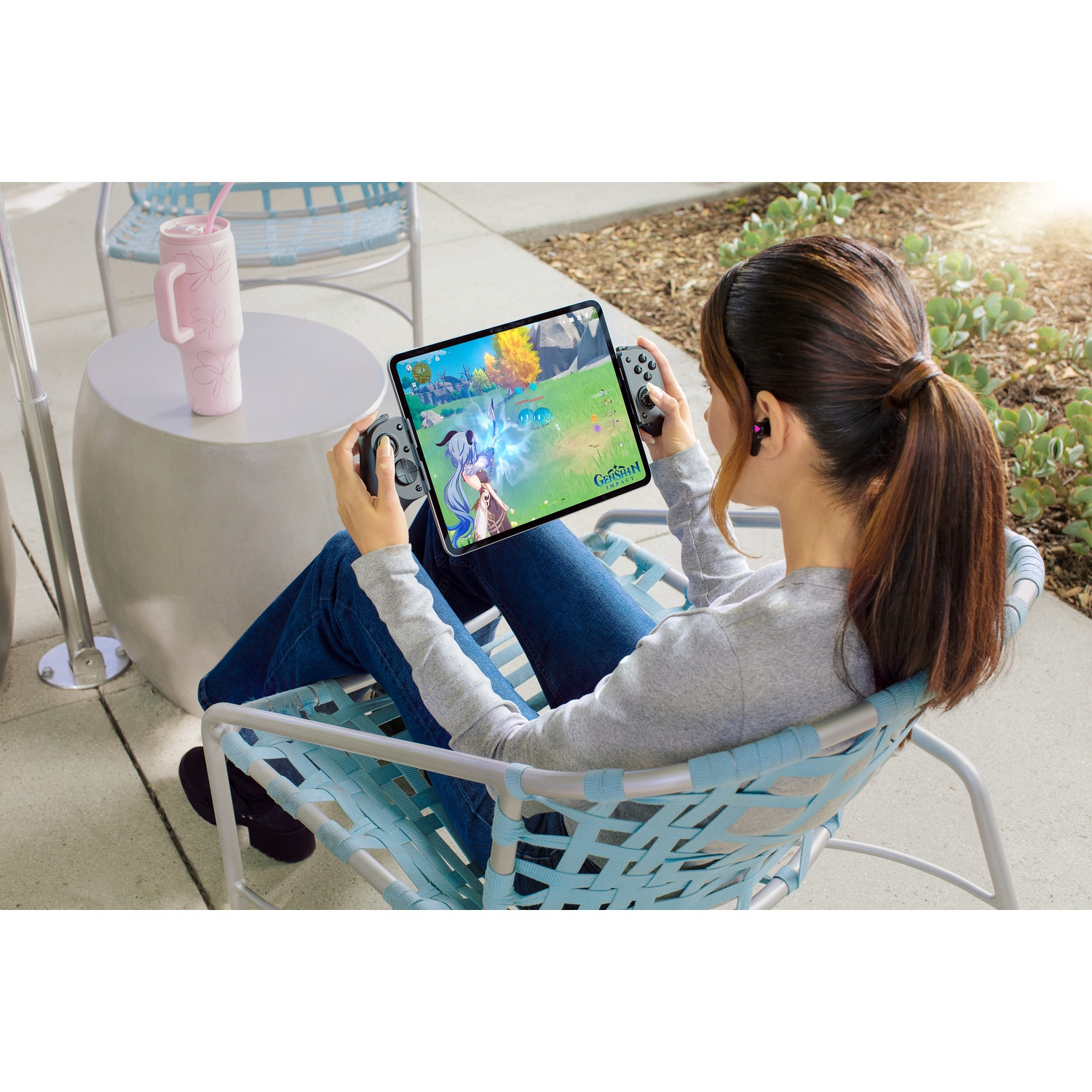 Een vrouw speelt een spel op een tablet in de buitenlucht. Ze zit in een blauwe stoel en houdt een controller vast.