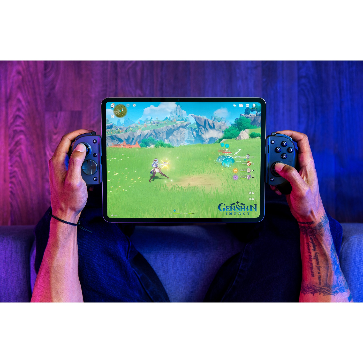 Een persoon speelt Genshin Impact op een tablet. De tablet wordt vastgehouden met aangesloten controllers. De scène toont een personage in een groen veld.