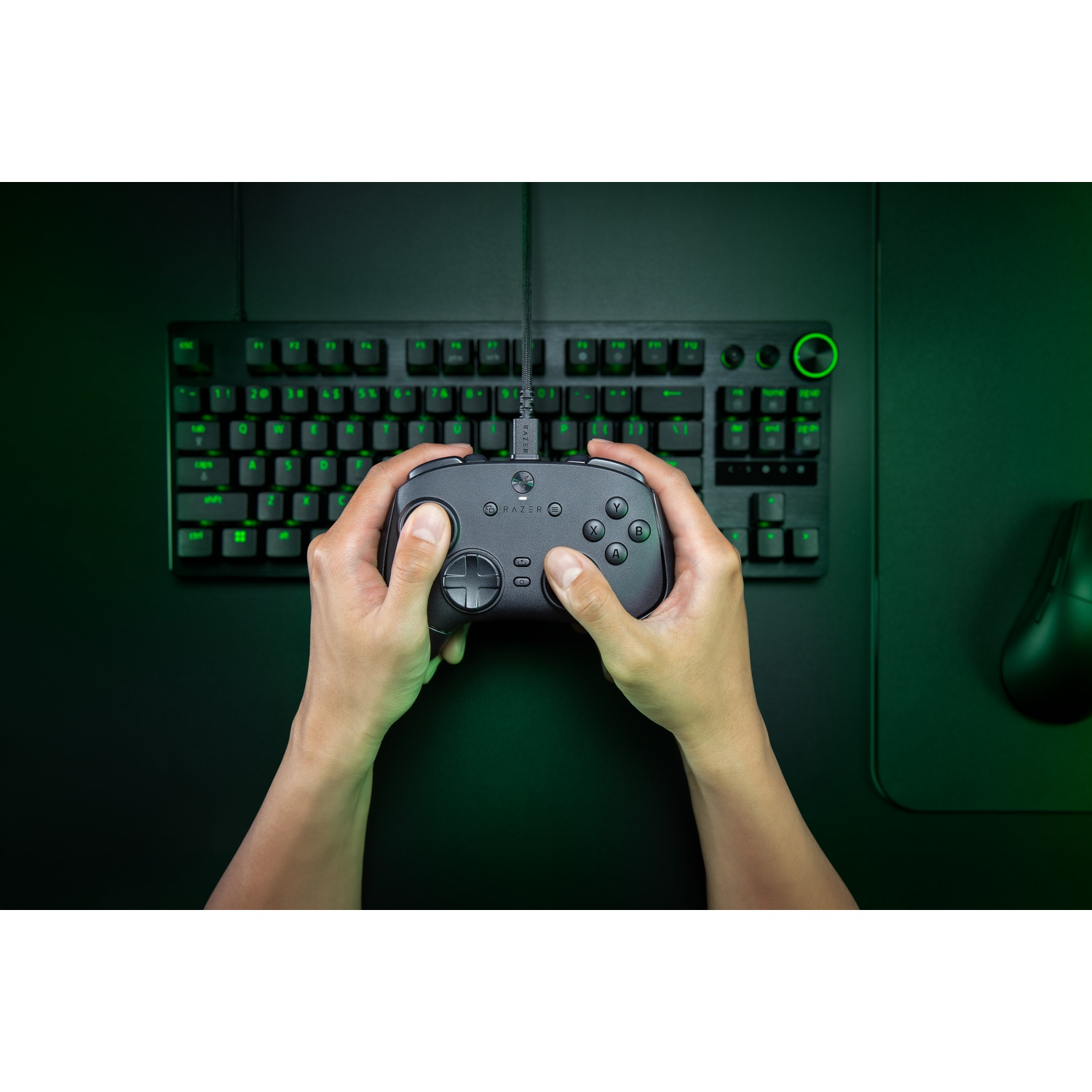 Hands holding a Razer controller over a black keyboard and mouse. Green-lit keys and a green gradient background.