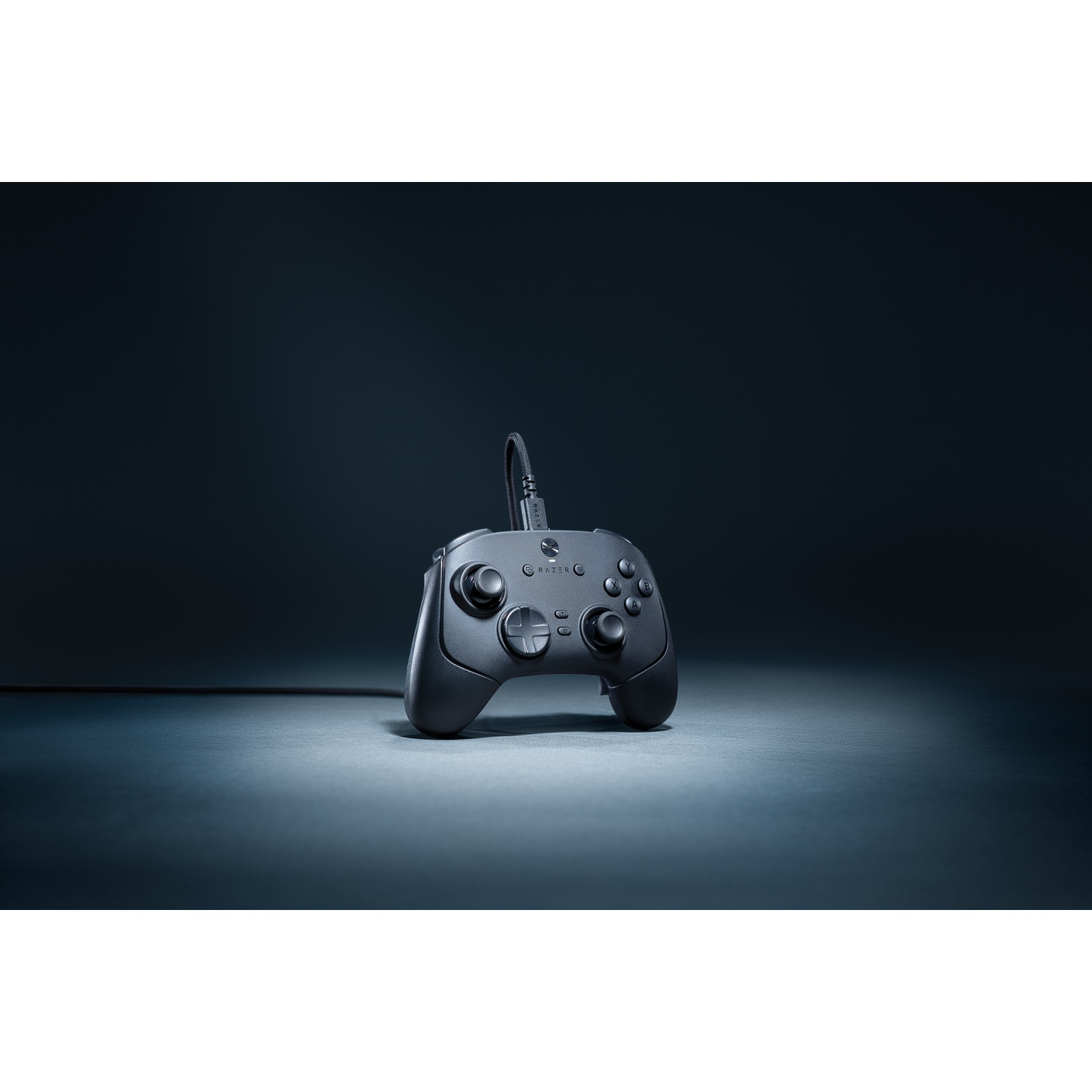A black Razer gamepad sits on a gray surface with a dark blue background. The gamepad has buttons and a wired connection.