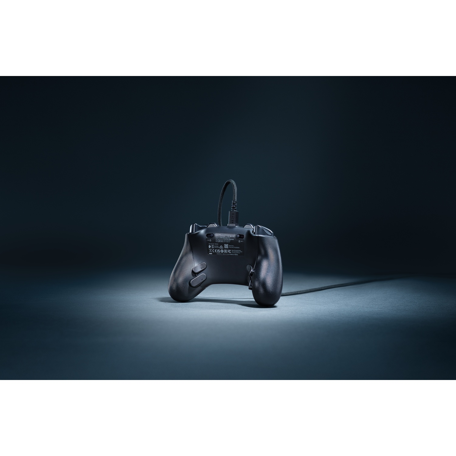 A black gamepad, back facing up, on a dark surface. A cable extends from the top of the gamepad.