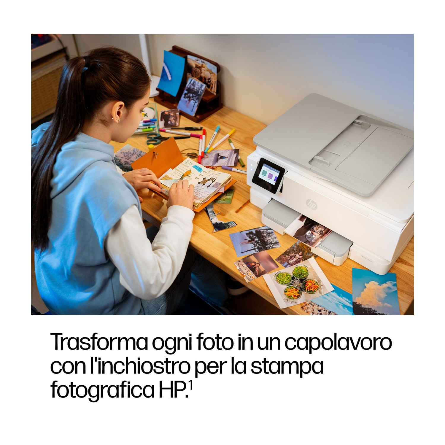 Una donna lavora a una scrivania con delle foto. Una stampante HP stampa foto. Ci sono pennarelli e un taccuino sulla scrivania.