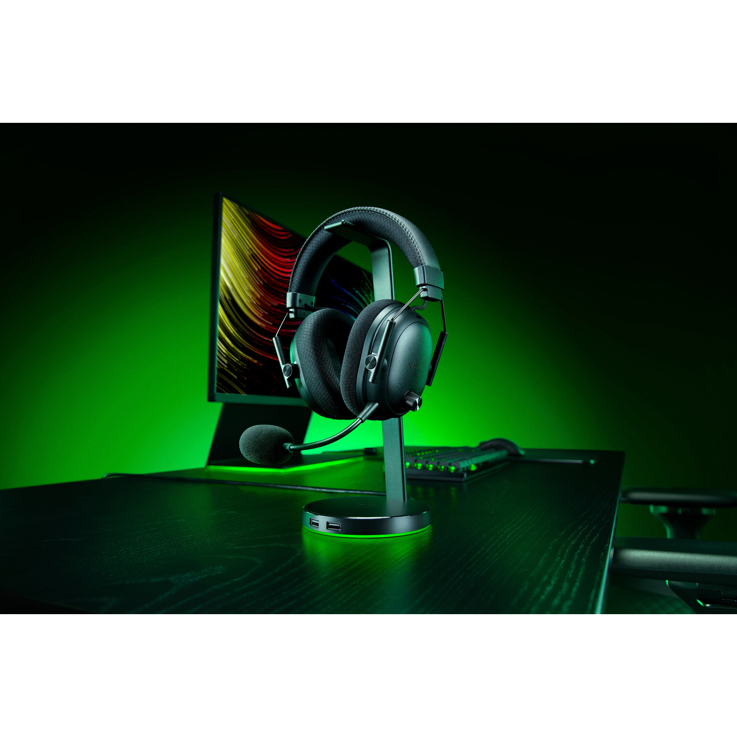 Black gaming headset on a stand, desk with keyboard, monitor with colorful abstract art, green background.