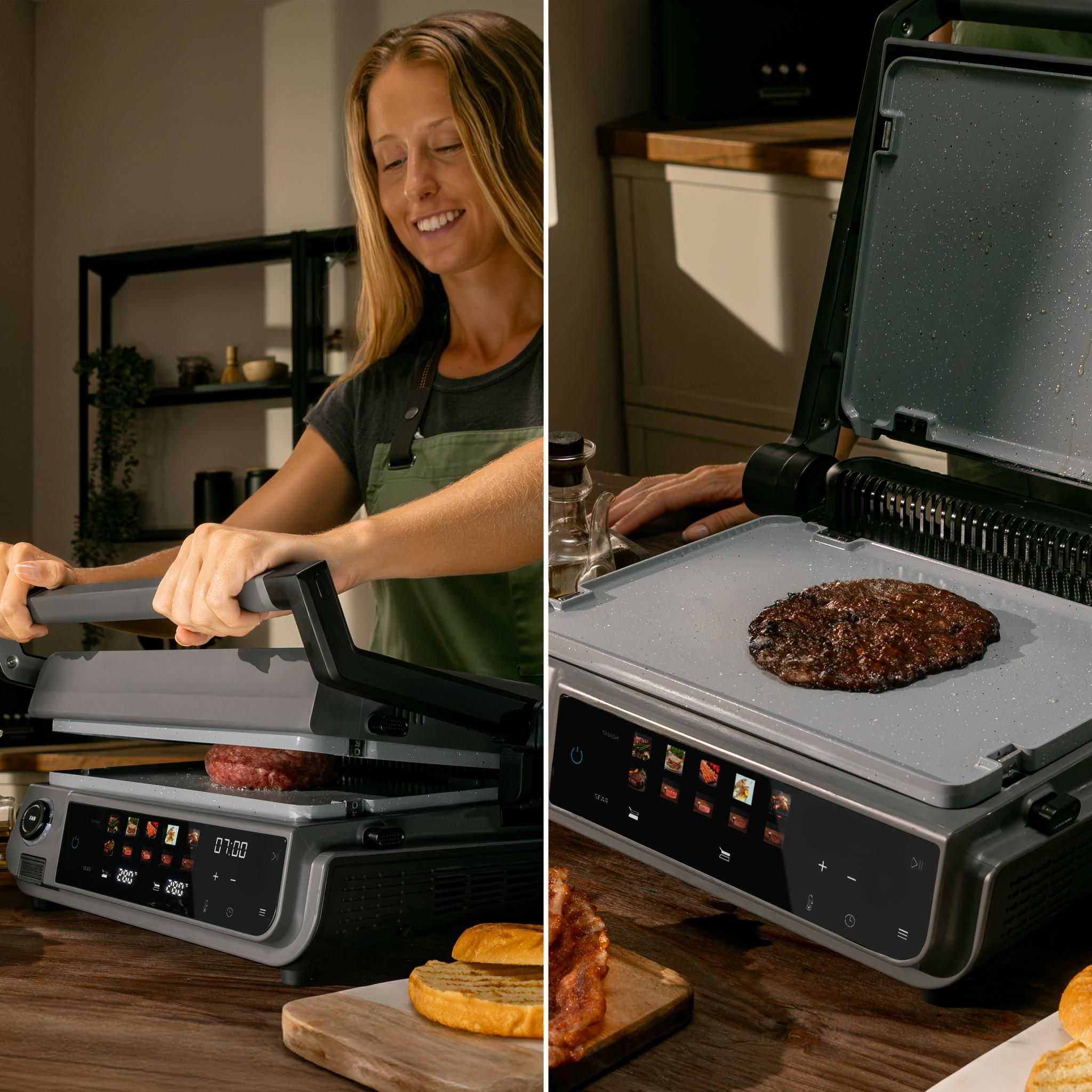 Mujer asando una hamburguesa en una parrilla. Hamburguesa cocinándose. Dos mitades de pan en tabla de madera. Cocina de fondo.