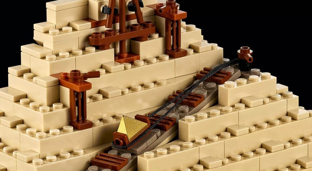 Piramida Lego z beżowymi klockami, brązowymi konstrukcjami i złotym elementem podnoszonym na linie.