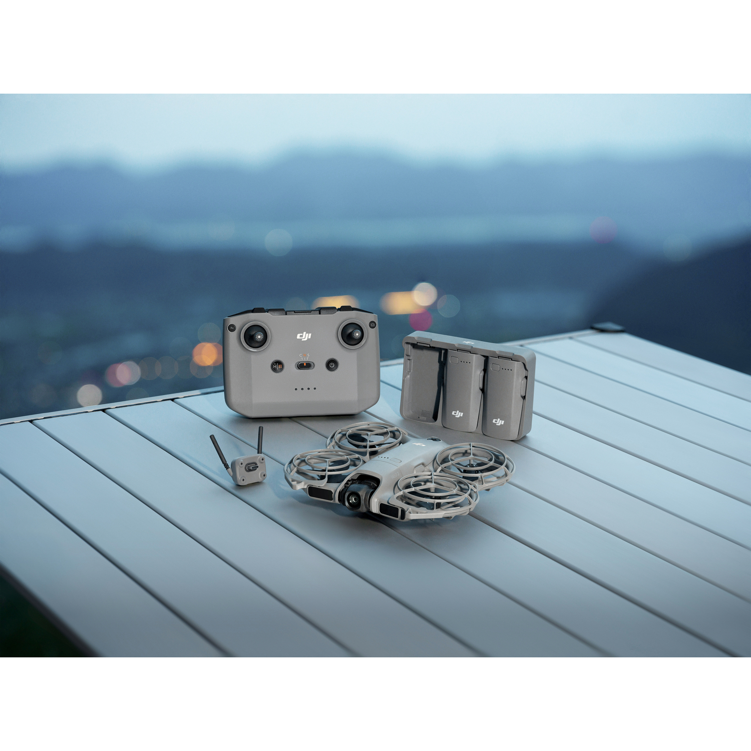 Dronekit op tafel. Inclusief drone, afstandsbediening, batterijen en oplader. Achtergrond toont een vage landschap met stadslichten.