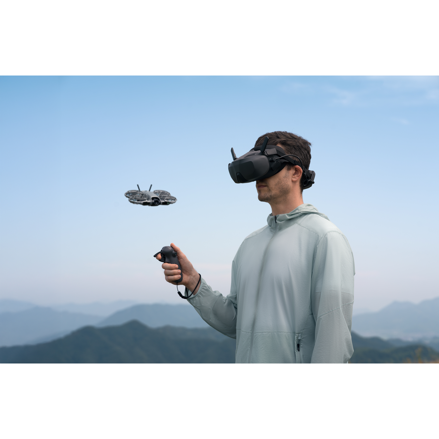 Een man met een VR-bril en controller bestuurt een drone in een berglandschap met blauwe lucht.