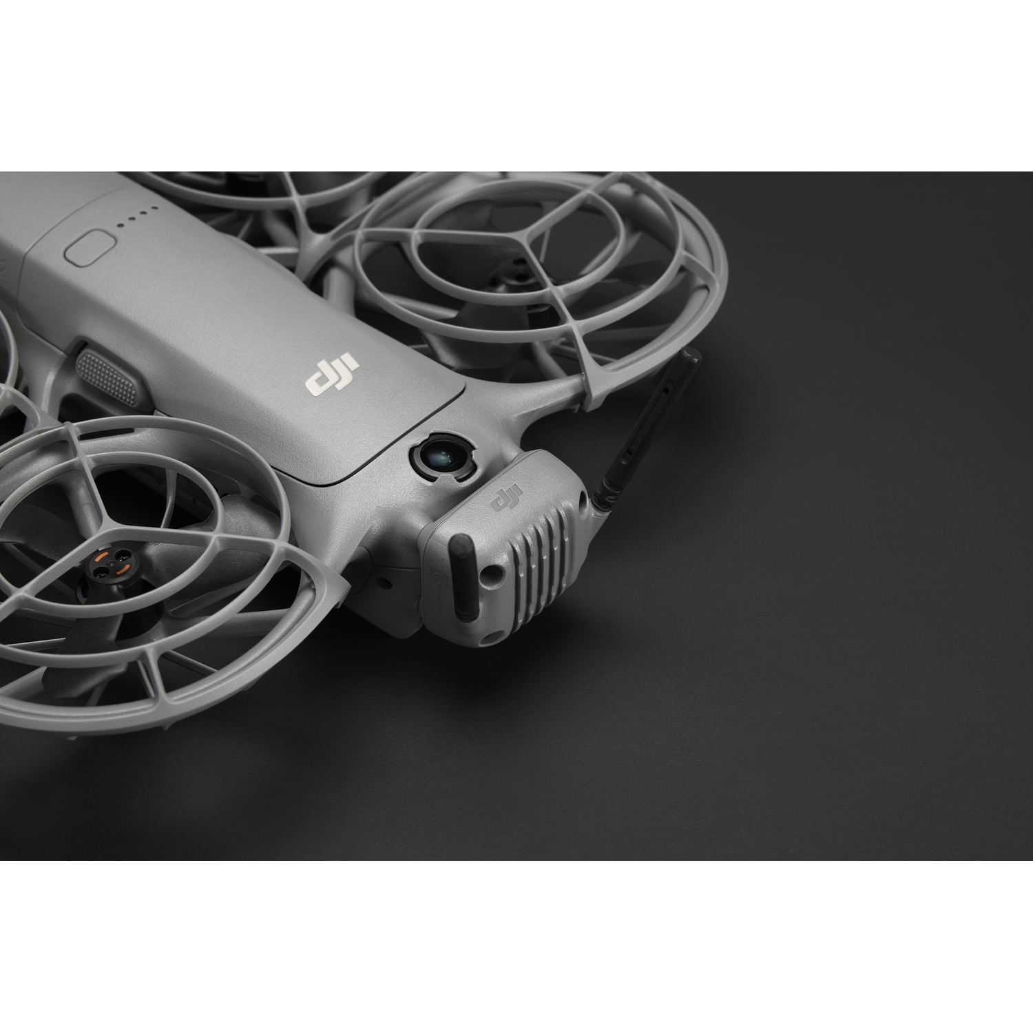 Een grijze drone met beschermende kooien rond de propellers ligt op een zwart oppervlak. Het DJI-logo is zichtbaar.
