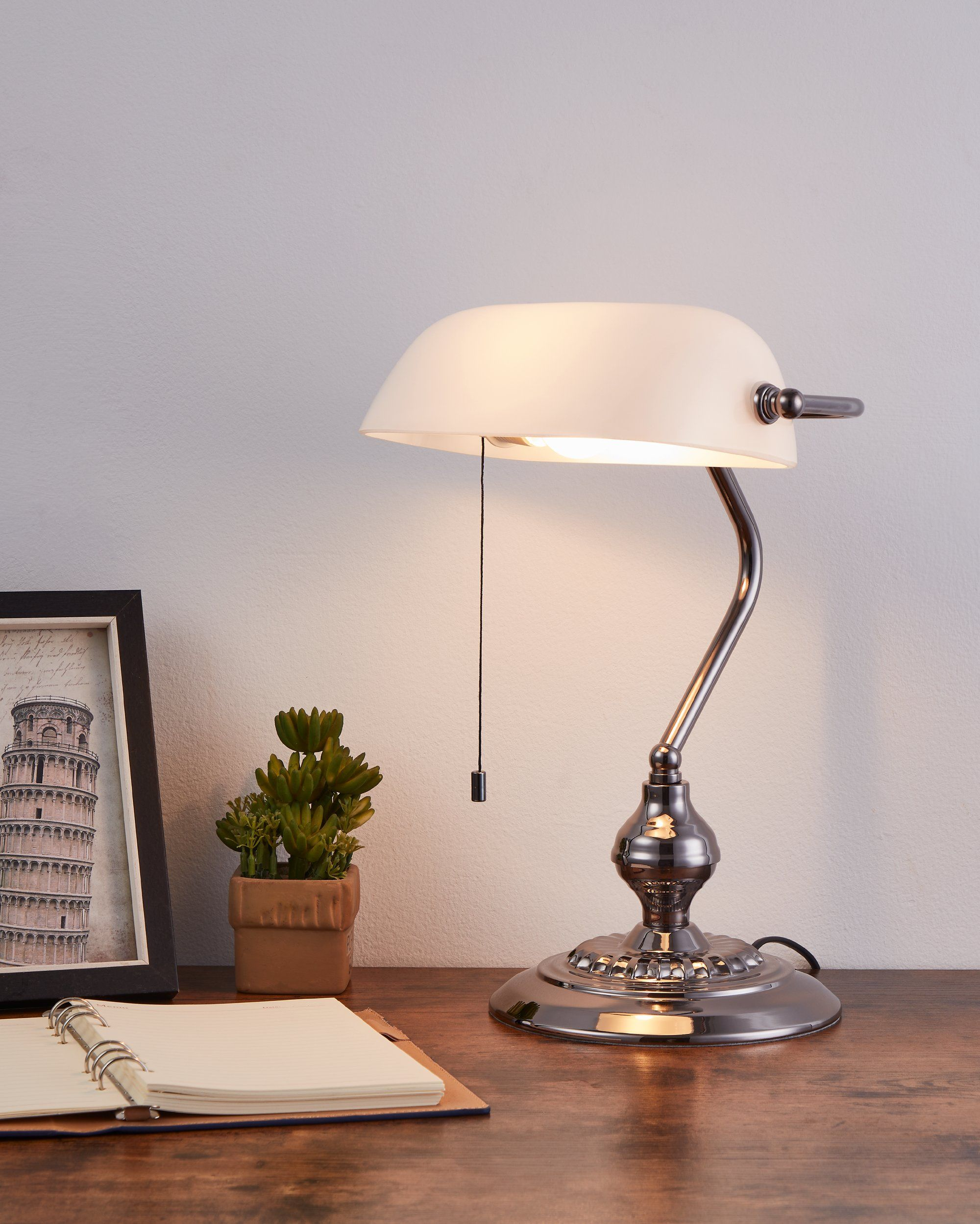 Ein Schreibtisch mit Lampe, Pflanze, Foto des Turms von Pisa und Notizbuch.
