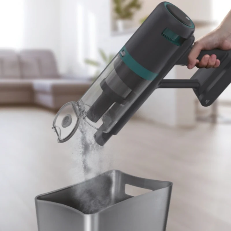Una persona sta svuotando un aspirapolvere portatile in un contenitore. L'aspirapolvere è nero e verde acqua. Il contenitore è grigio.
