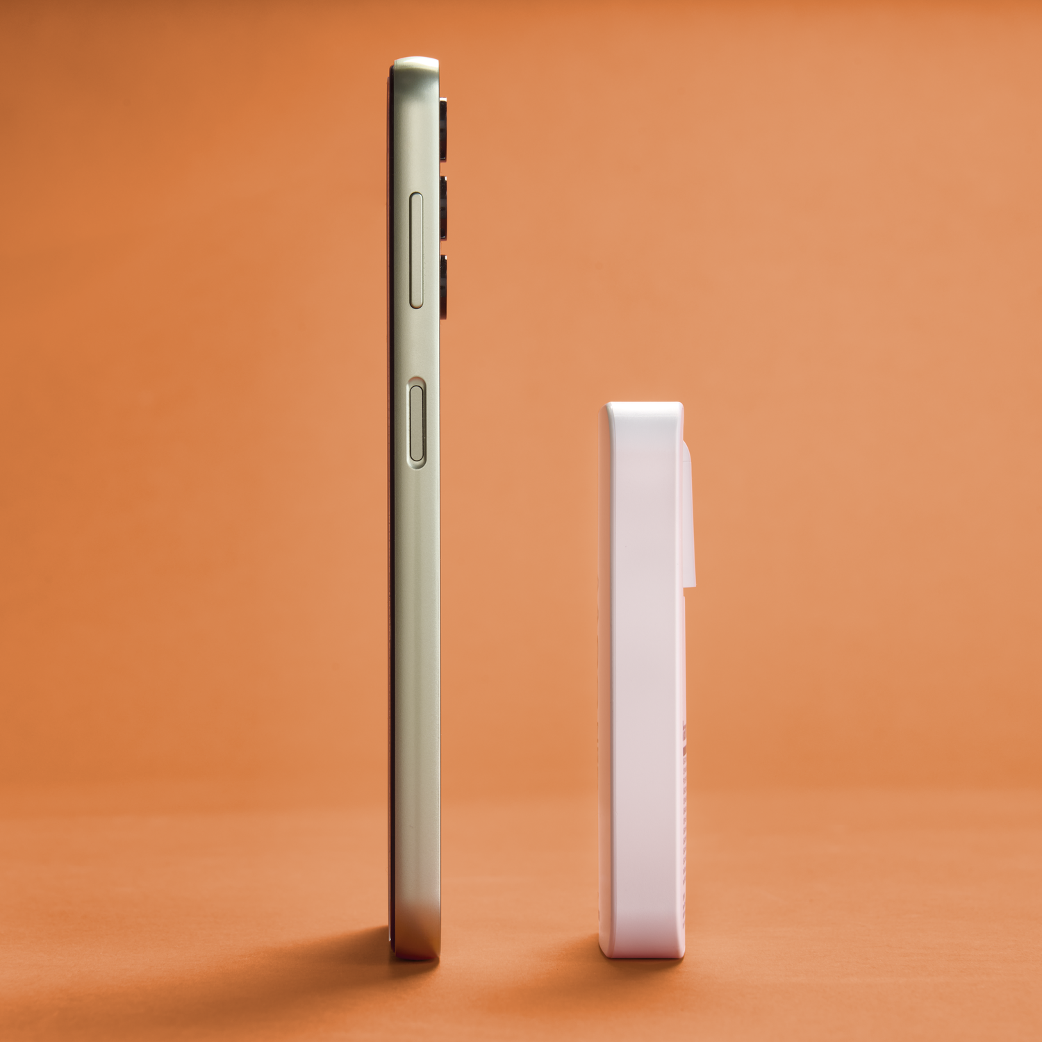 A smartphone and a white device stand side by side on an orange background. The phone is silver, and the device is rectangular.