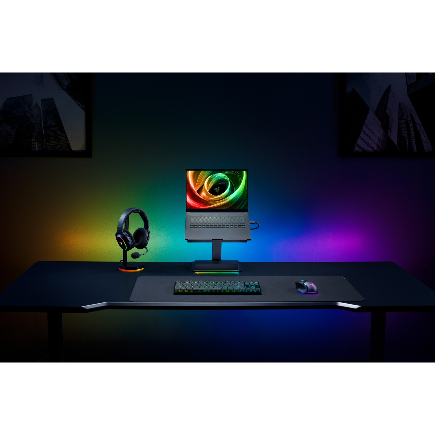 A gaming setup with a laptop, keyboard, mouse, and headset on a black desk. Colorful lights illuminate the background.