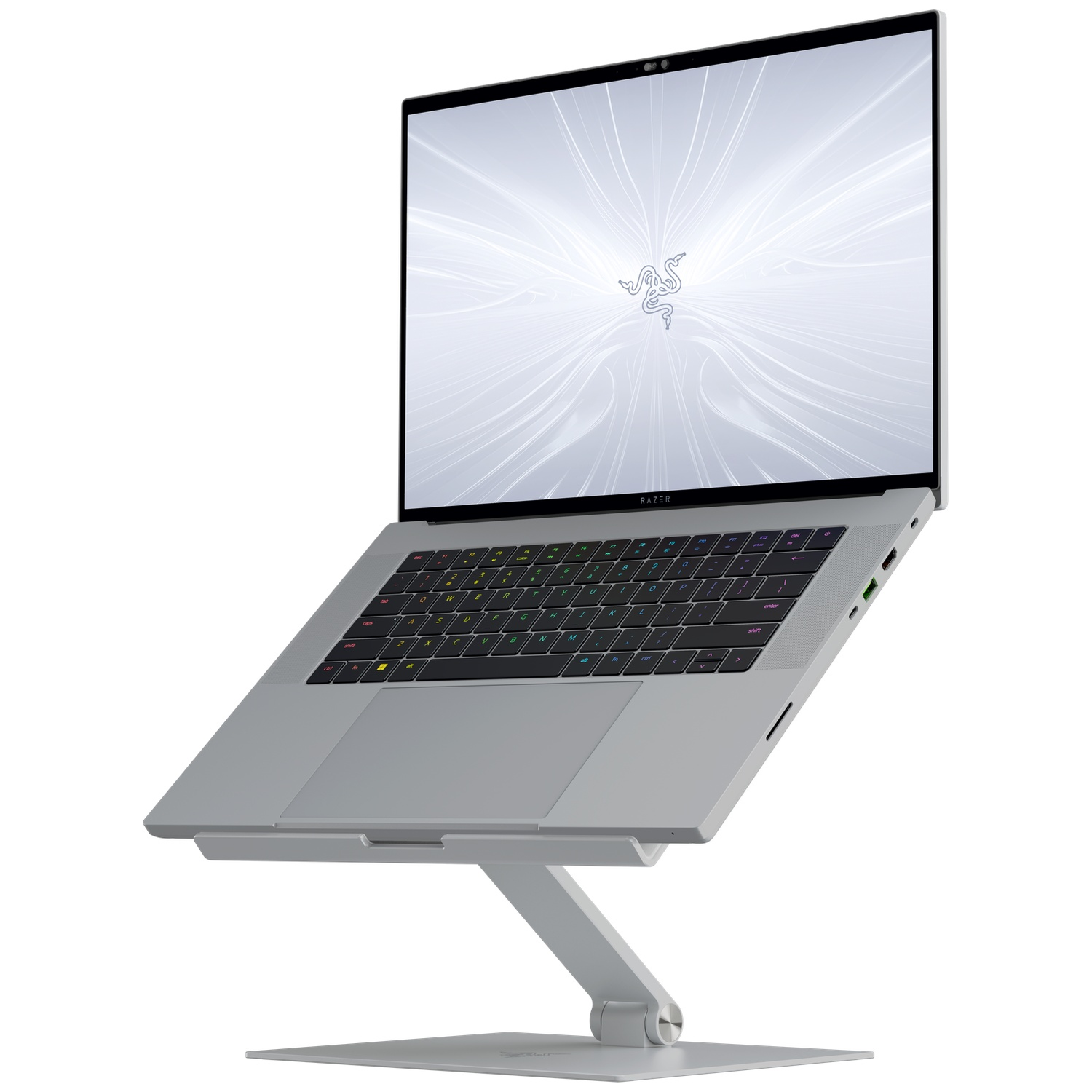 A gray laptop on a stand. The screen displays a Razer logo. The keyboard is backlit in multiple colors.