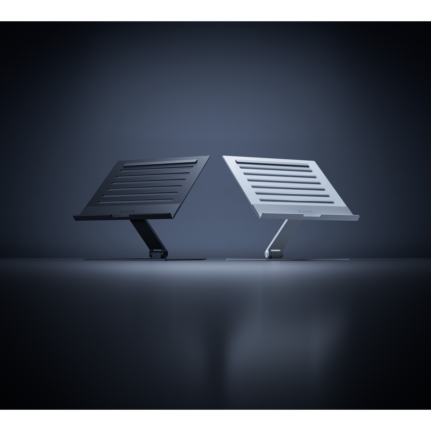 Two laptop stands, one black and one silver, are positioned facing each other on a dark surface. The stands have a Razer logo.