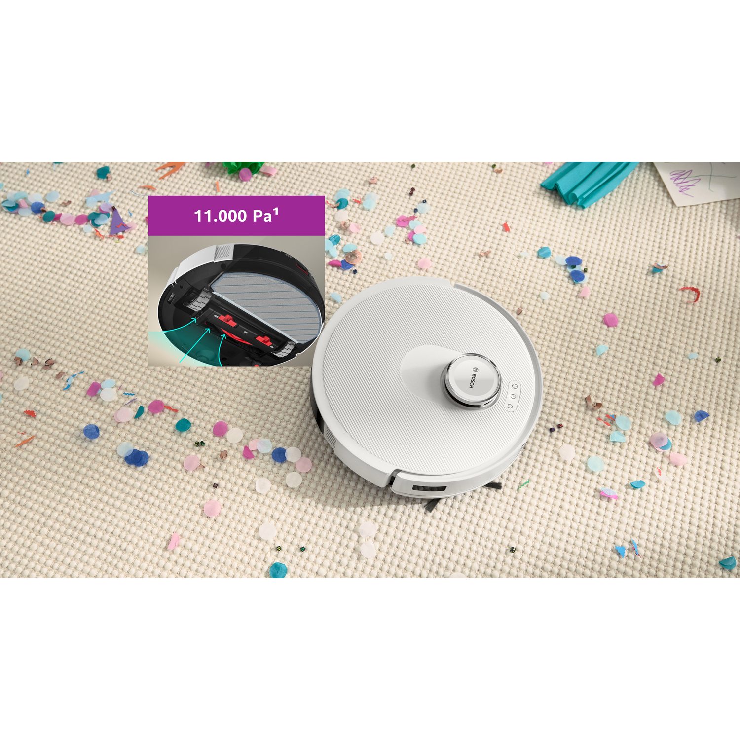 A white robot vacuum cleaner on a beige carpet scattered with colorful confetti. An inset shows the vacuum's internal brush.