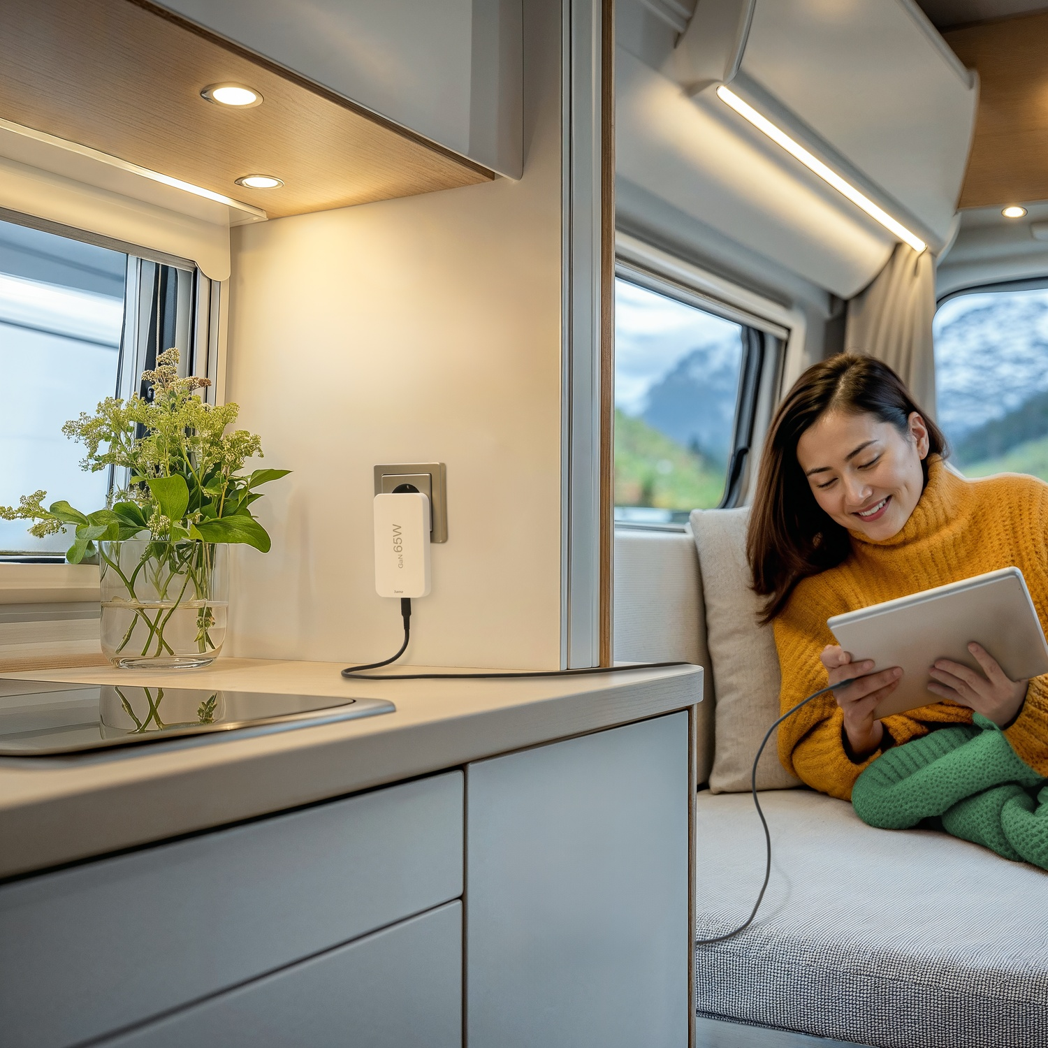 Femme dans un camping-car utilisant une tablette. Un chargeur est branché au mur. Un vase avec des fleurs est sur le comptoir.