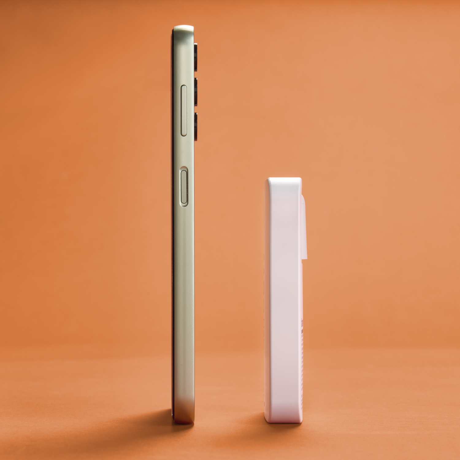 Un smartphone et un appareil rectangulaire blanc se tiennent côte à côte sur un fond orange. Le téléphone est argenté.