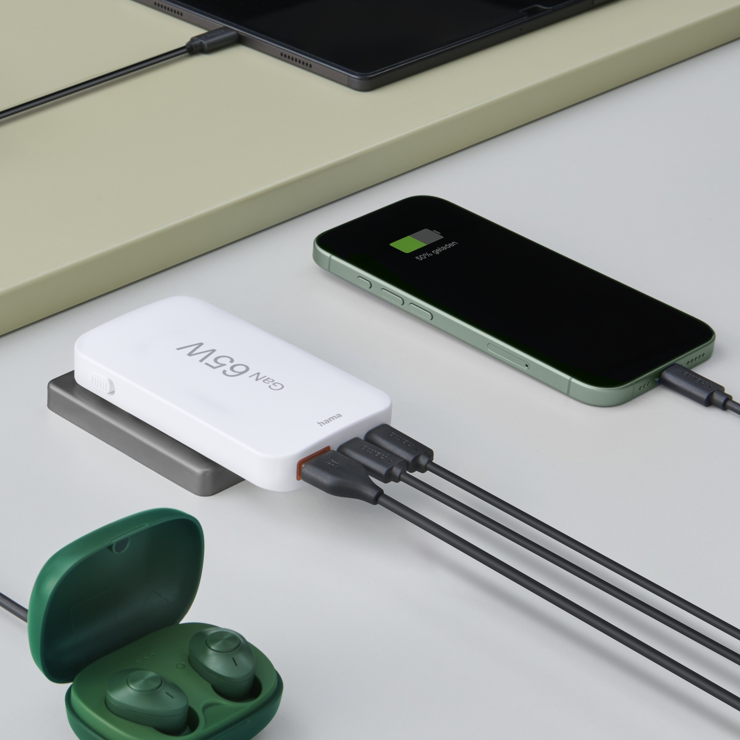 Une batterie externe blanche avec trois câbles de charge connectés à un téléphone, une tablette et des écouteurs. Le téléphone affiche 50% de charge.