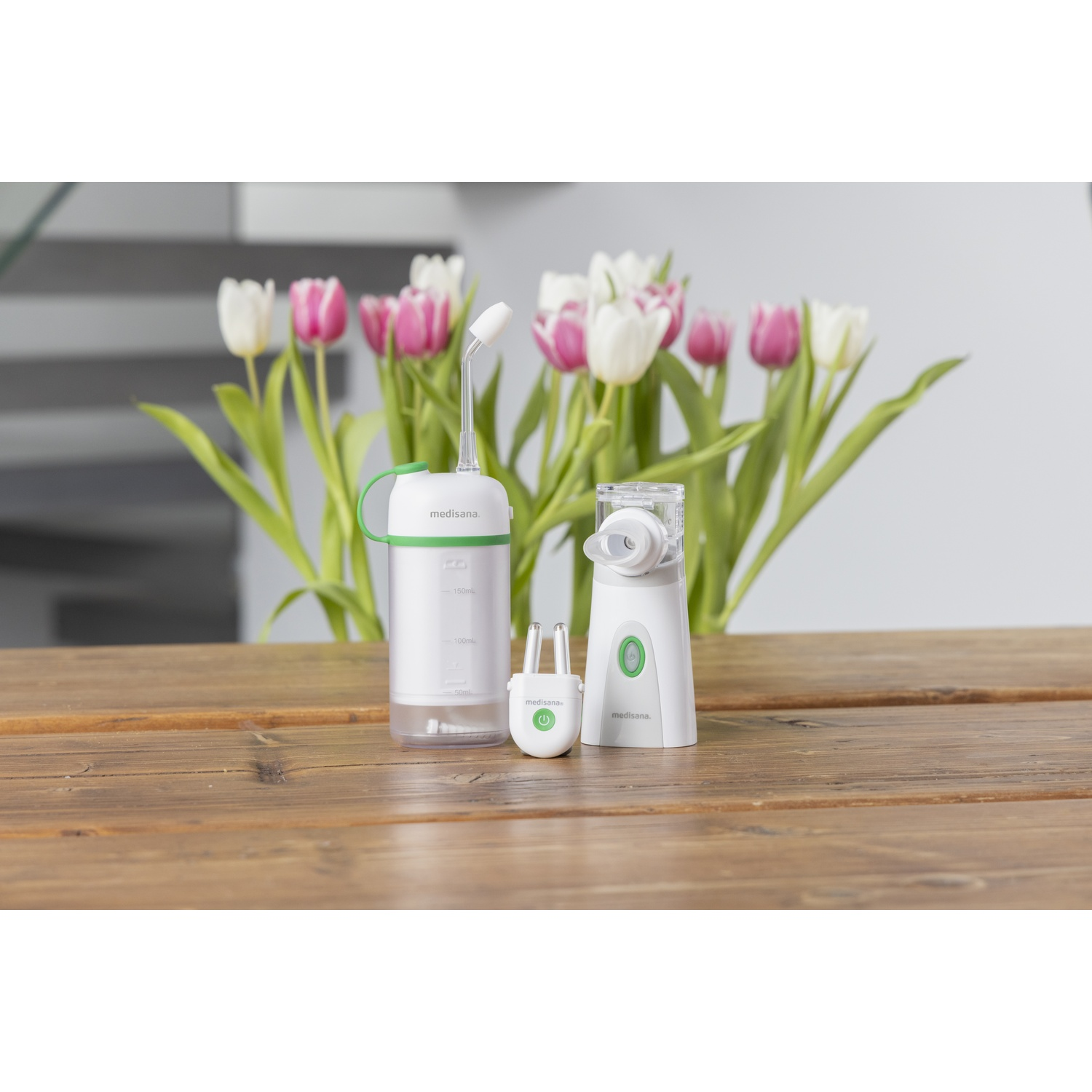 Three white and green medical devices on a wooden table, with a tulip bouquet in the background.