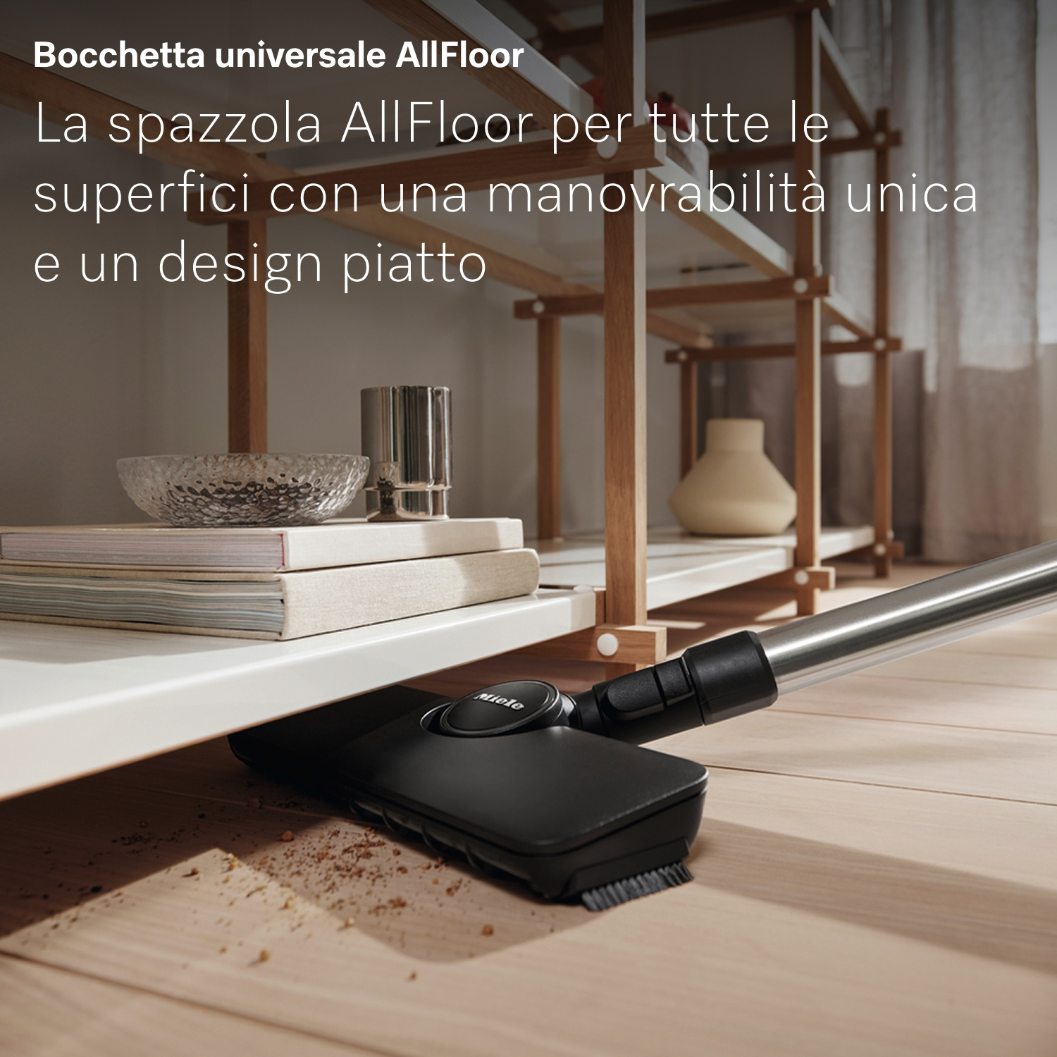 Una testina nera per aspirapolvere pulisce un pavimento in legno. Mensole e oggetti sullo sfondo.