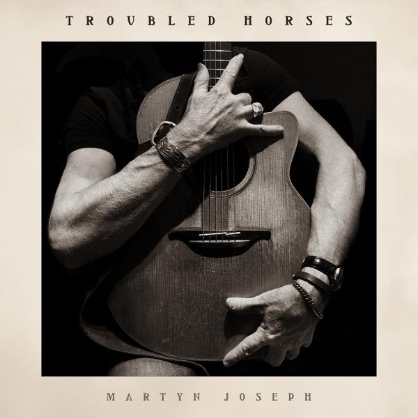 Schwarz-Weiß-Bild von Händen, die eine Gitarre halten. Der Künstler, Martyn Joseph, ist zu sehen. Der Albumtitel lautet 'Troubled Horses'.