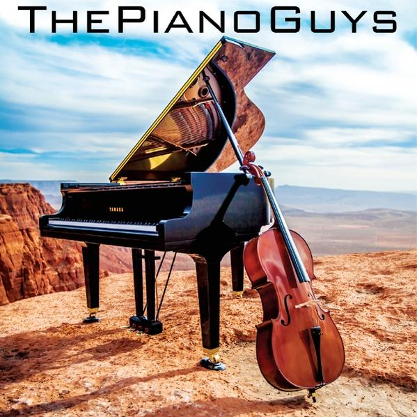 Ein Flügel und ein Cello stehen auf einer roten Felsformation mit Bergkulisse und blauem Himmel. Das Logo The Piano Guys ist oben.