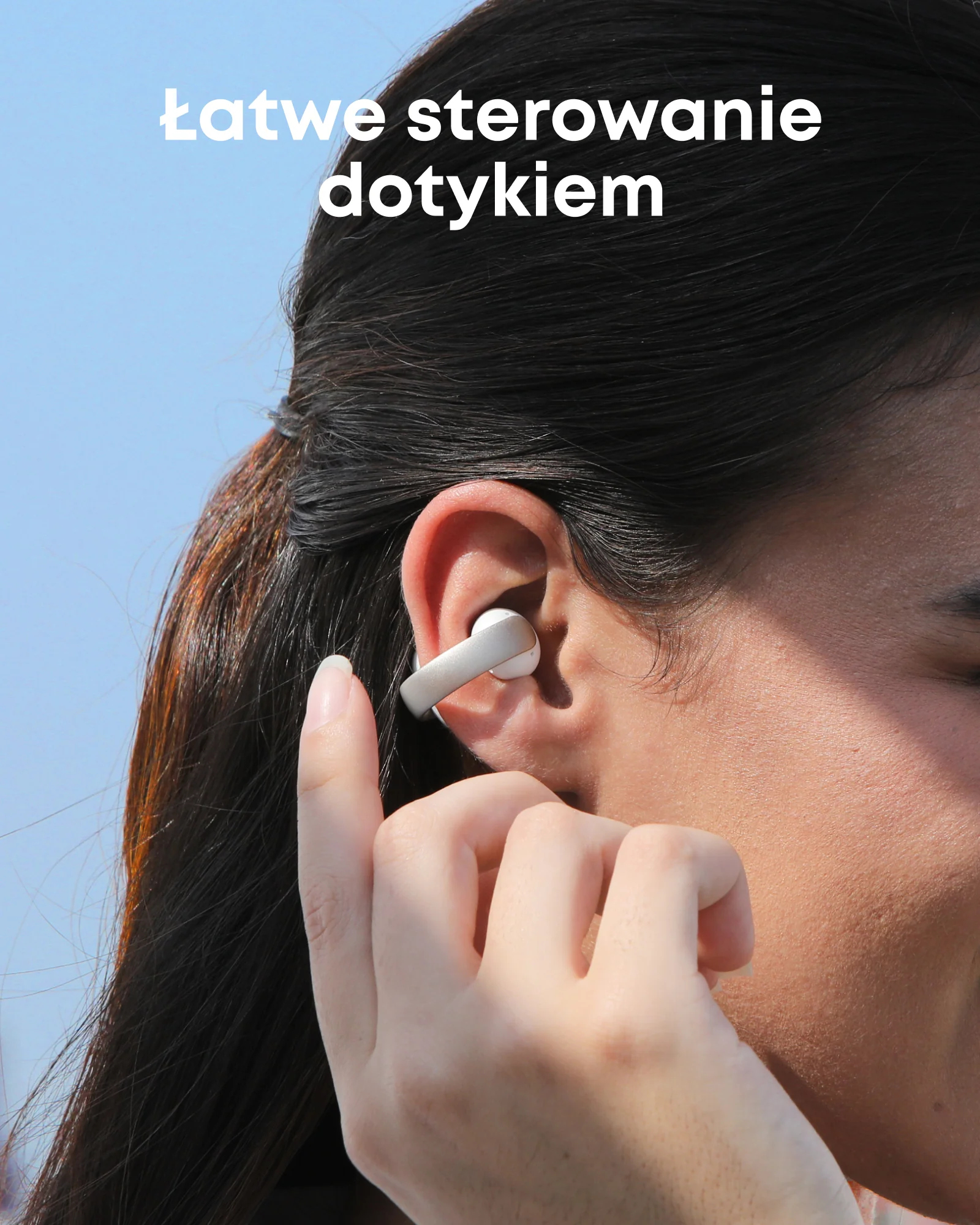 Kobieta z wkładką douszną dotyka ucha. Tekst: łatwe sterowanie dotykiem. Tło niebieskiego nieba.