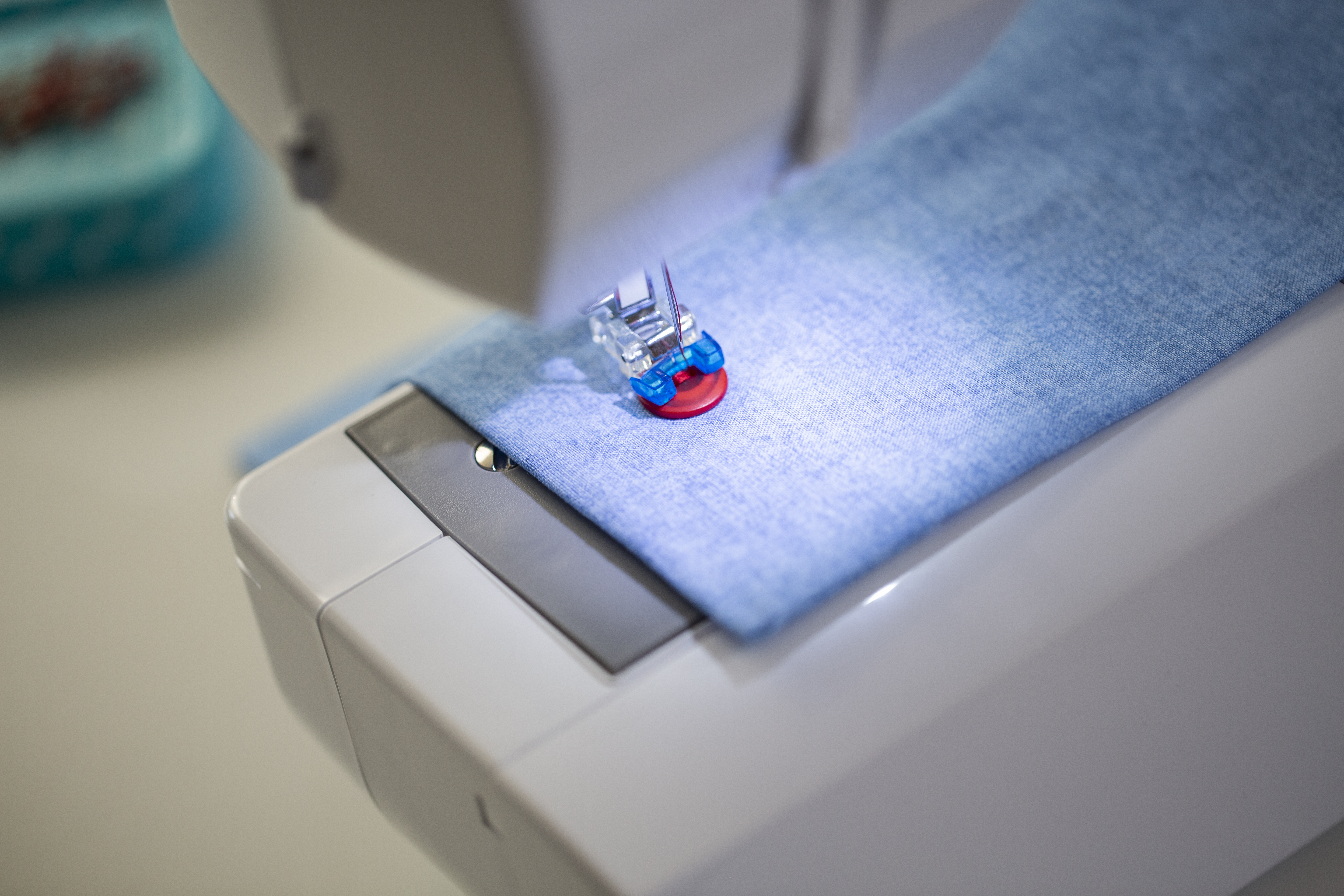 Nähmaschine mit blauem Stoff. Der Nähfuß ist unten. Die Maschine ist weiß mit grauen Akzenten.