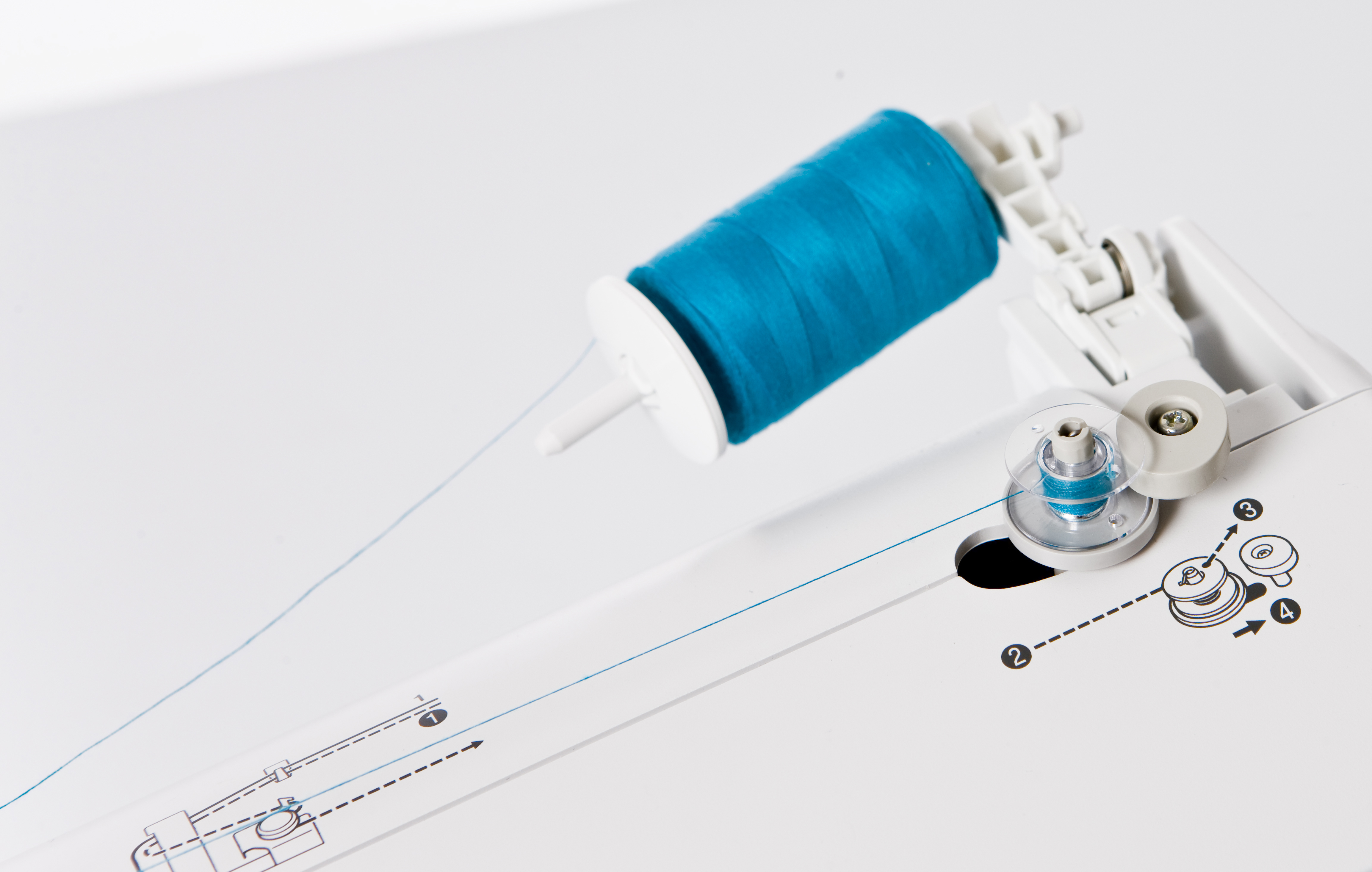 Detail der Nähmaschine. Blauer Faden auf einer Spule. Weiße Maschinenteile und Anweisungen auf weißer Oberfläche.