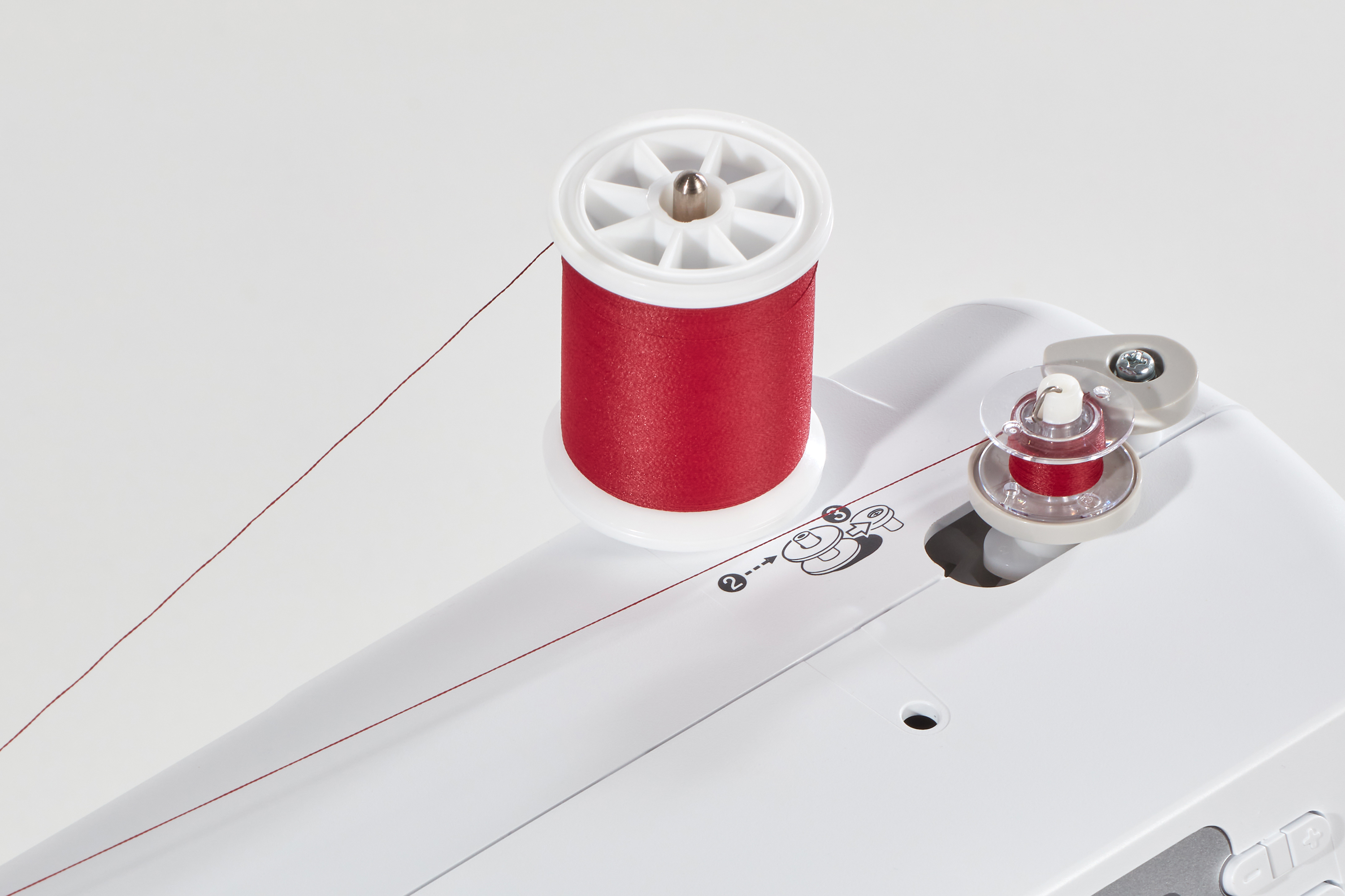 Nähmaschine mit roter Garnspule und Spule. Weiße Maschine mit rotem Faden und weißem Hintergrund.