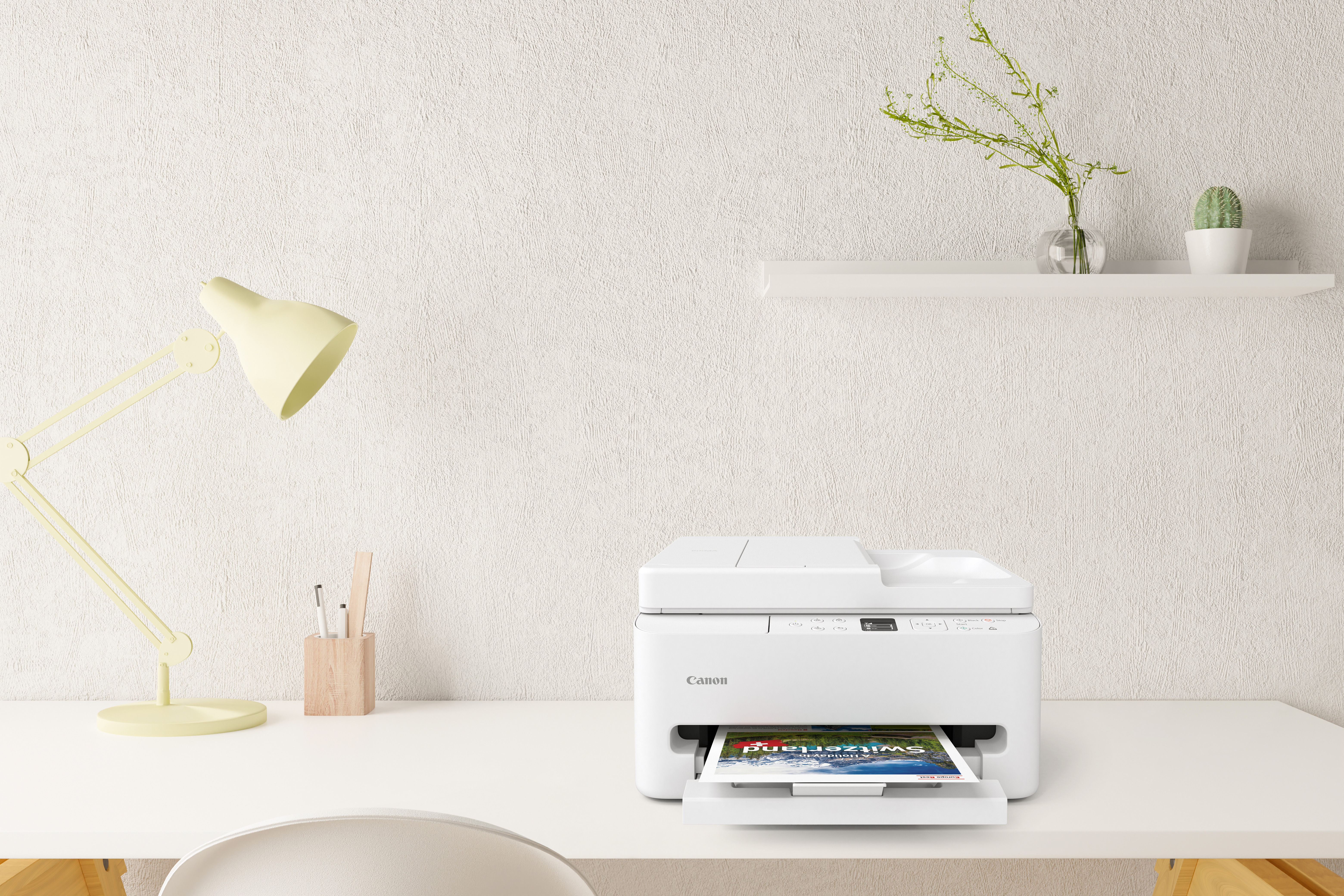 Biała drukarka Canon na białym biurku, z żółtą lampą, długopisami i półką.