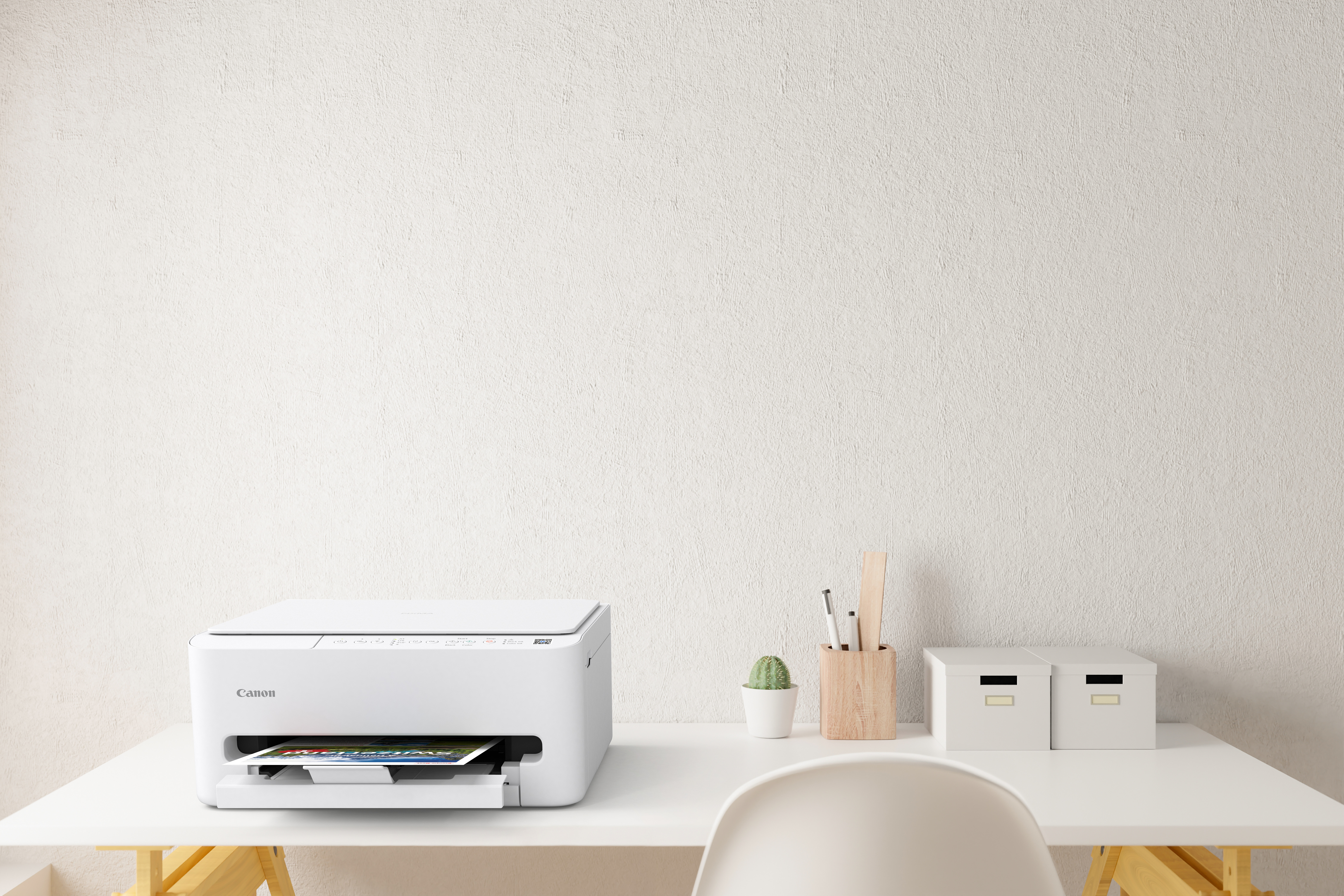 Biała drukarka na białym biurku z artykułami piśmienniczymi i pudełkami. Obecny jest również kaktus.
