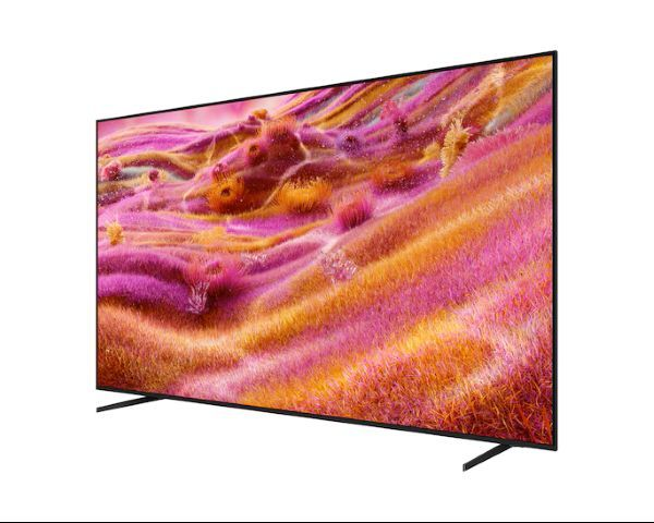 Büyük, siyah çerçeveli bir TV, beyaz bir arka plan üzerinde pembe, turuncu ve sarı tonlara sahip renkli, soyut bir manzara görüntülüyor.