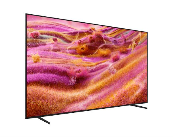 Büyük bir TV, pembe, turuncu ve sarı tonlarında renkli, soyut bir manzara gösteriyor, siyah bir stand üzerine monte edilmiş.