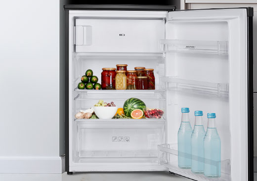 Otwarta lodówka wypełniona słoikami, warzywami, owocami i butelkami wody. Zawiera arbuza i miskę jedzenia.