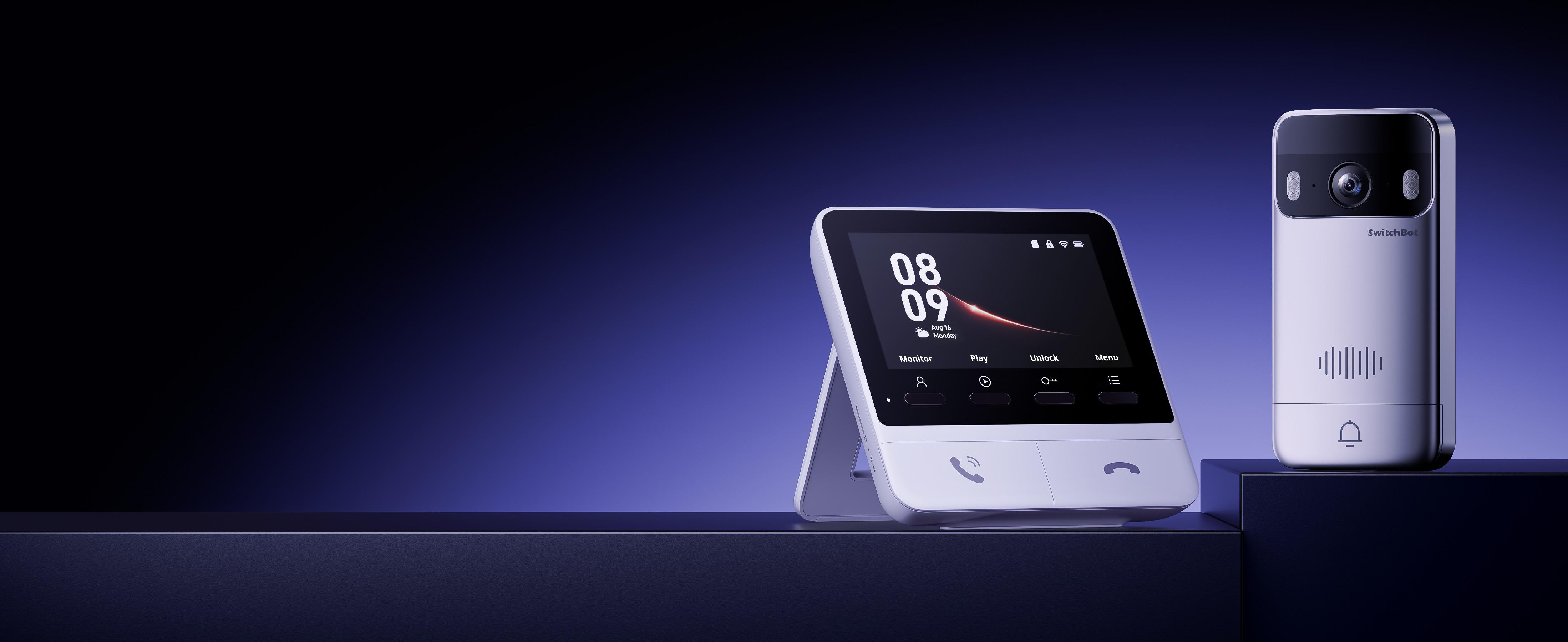 Ein Smart-Home-Gerät. Ein Bildschirm zeigt Uhrzeit und Menü an. Rechts befindet sich eine Kamera. Beides steht auf dunkler Oberfläche.