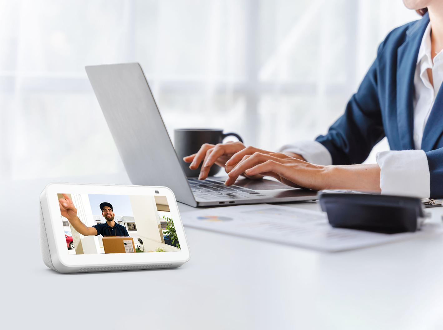 Eine Person telefoniert per Video mit einem Zusteller, der ein Paket hält, während sie an einem Laptop arbeitet.