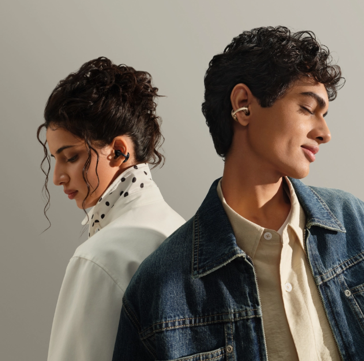 Dwie osoby w słuchawkach, tyłem do siebie. Jedna w dżinsowej kurtce, druga w białej koszuli w czarne kropki.