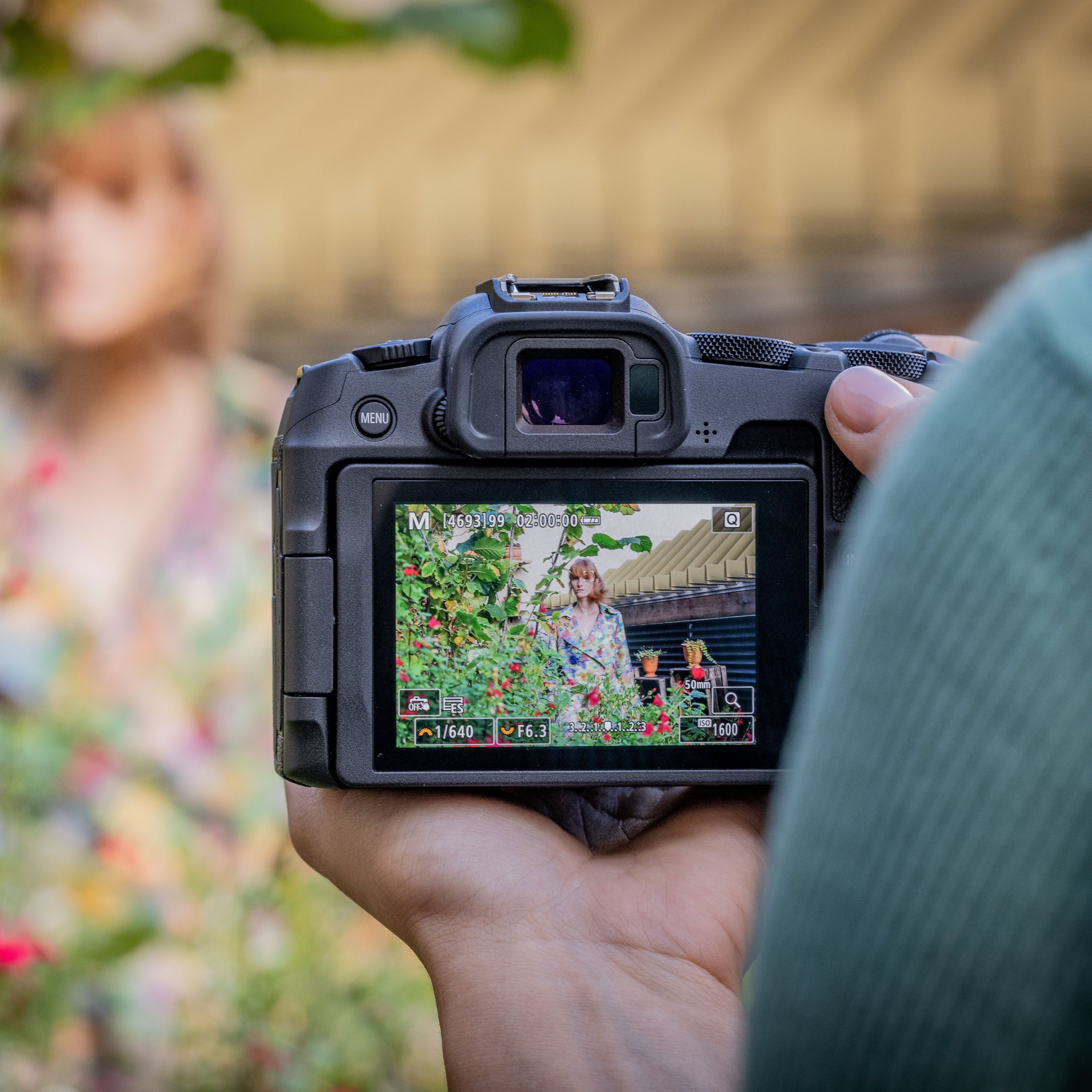 Une personne tient un appareil photo, l'écran montre un mannequin dans un jardin. Le mannequin porte une chemise fleurie.