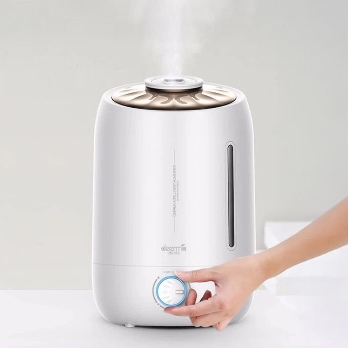 Biały nawilżacz z dłonią regulującą pokrętło. Para unosi się z góry. Marka to 'deerma'.