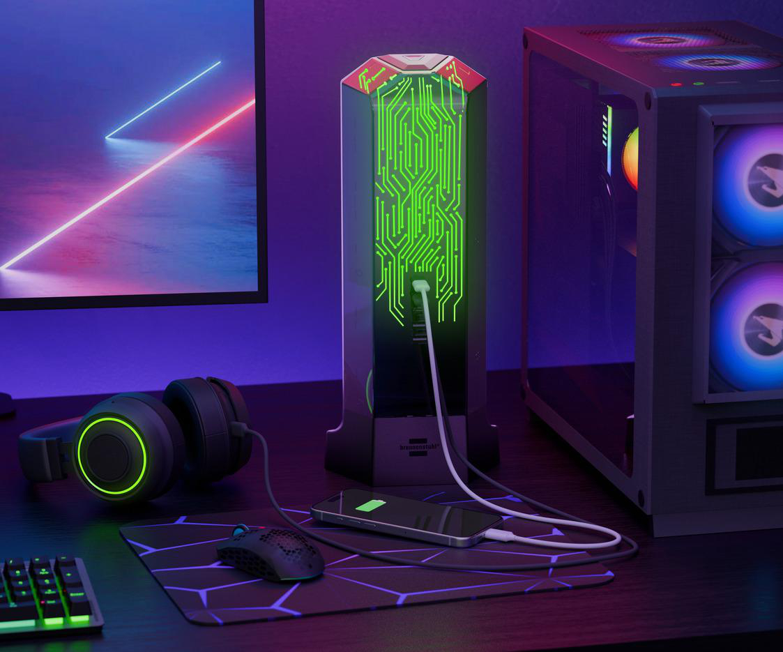 Gaming-Setup mit Kopfhörern, PC und ladendem Telefon. Leuchtendes grünes Leiterplattendesign auf einem schwarzen Turm. Lila und blaue Beleuchtung.