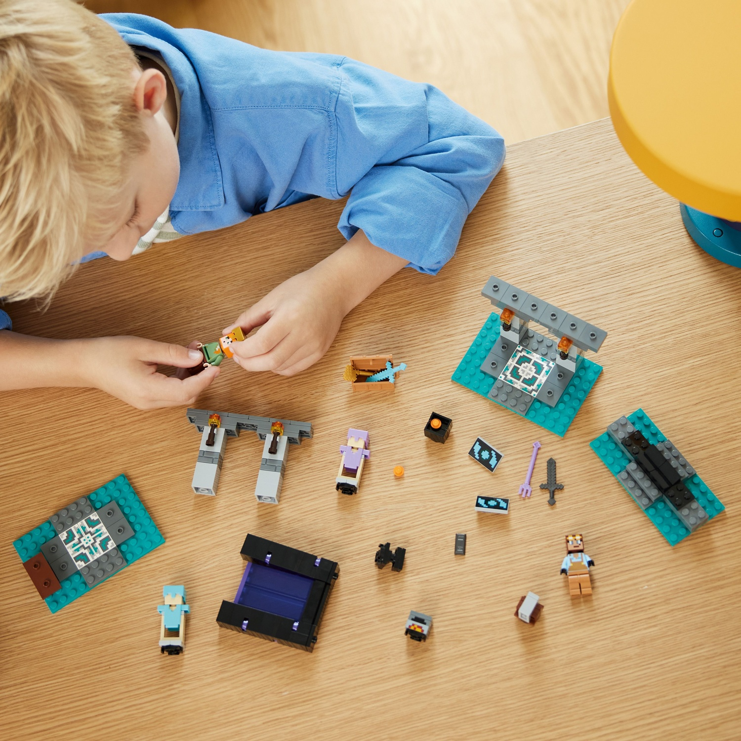 Een kind speelt met Lego Minecraft figuren. Verschillende stukken en karakters liggen verspreid op een houten tafel. Het kind is geconcentreerd.