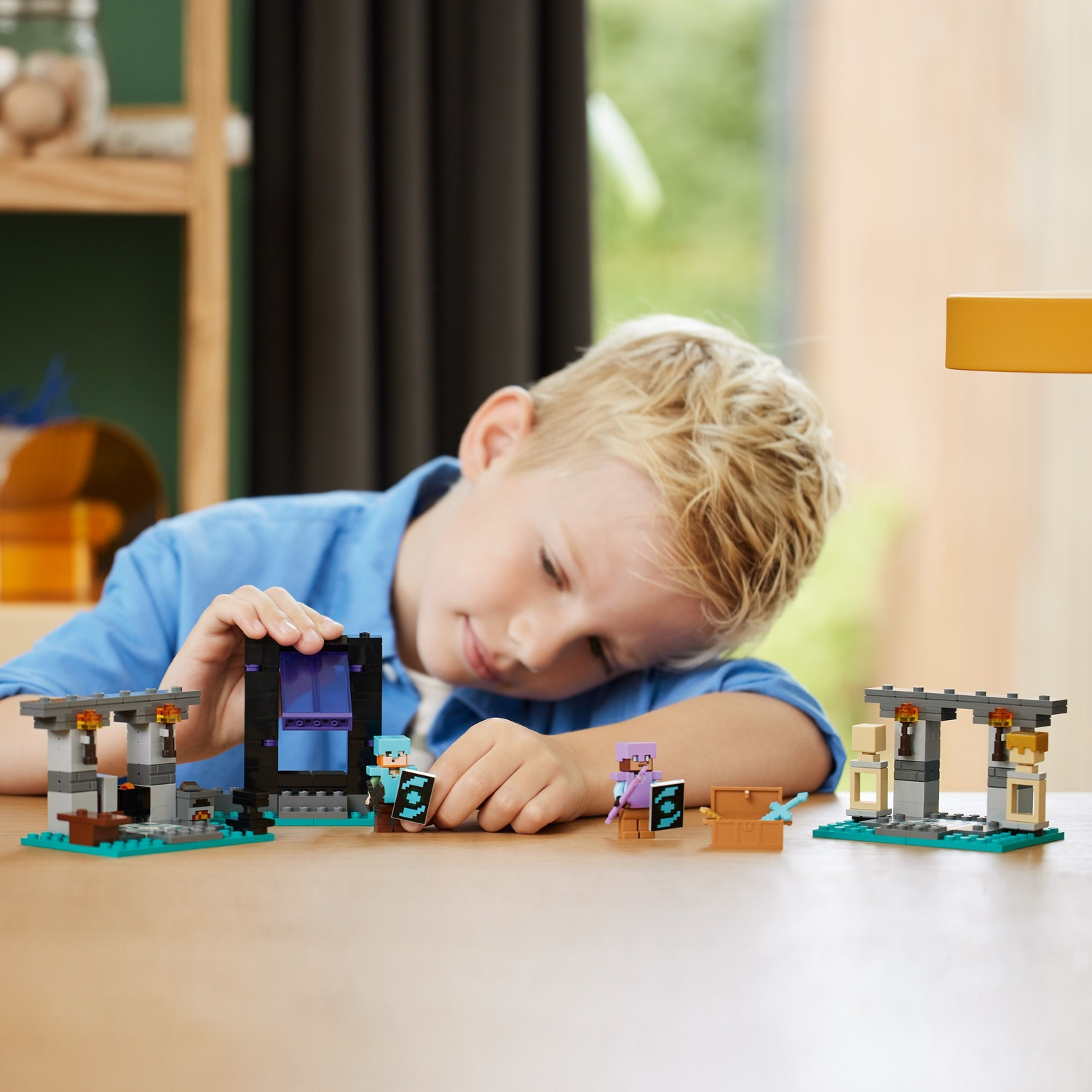 Een jongen met blond haar leunt op een tafel en speelt met Minecraft Lego. Sets en minifiguren zijn op de tafel geplaatst.