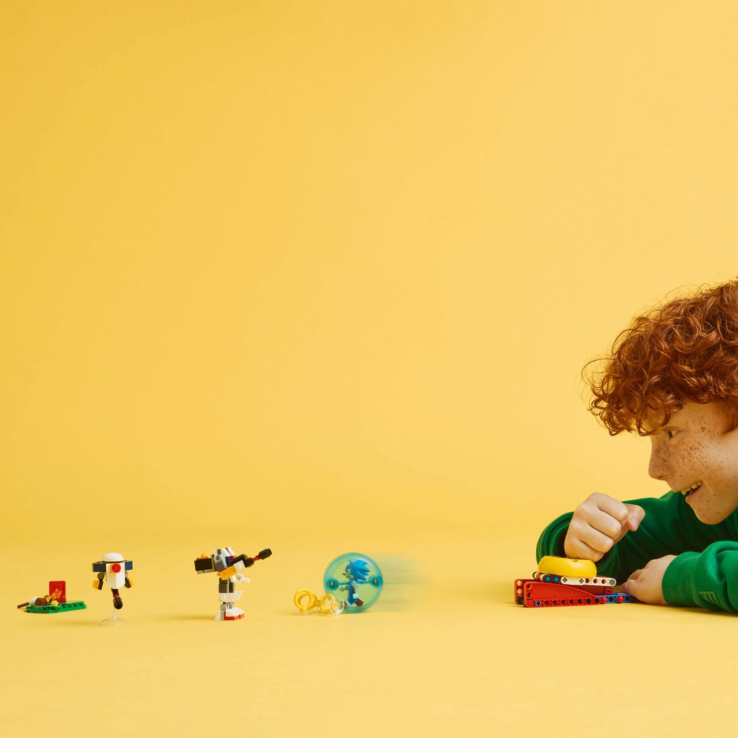 Een jongen met rood haar speelt met Lego Sonic-figuren op een gele achtergrond. Figuren zijn onder andere Sonic in een bal.
