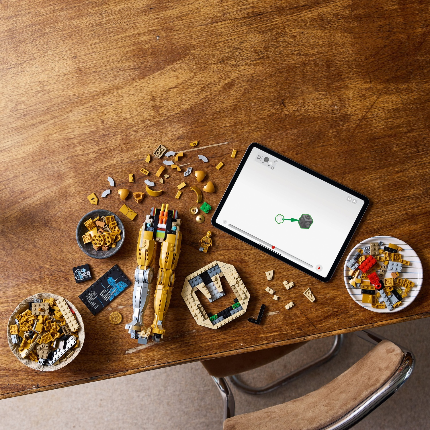 Wooden table with Lego pieces, instructions, tablet showing assembly, bowls of bricks, and a partially built figure.