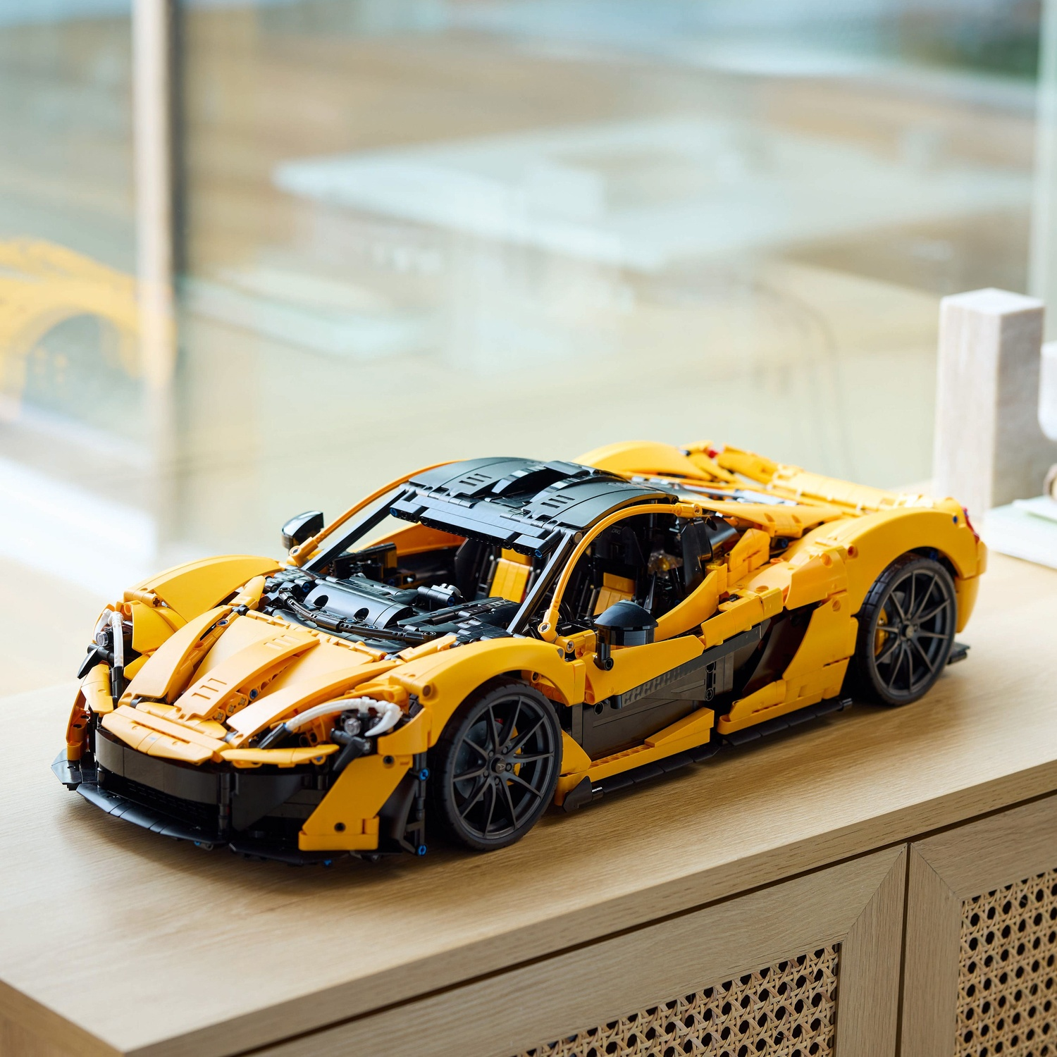 Een gele en zwarte Lego sportwagen staat op een houten oppervlak. De auto is gedetailleerd, met zwarte wielen en een strak design.