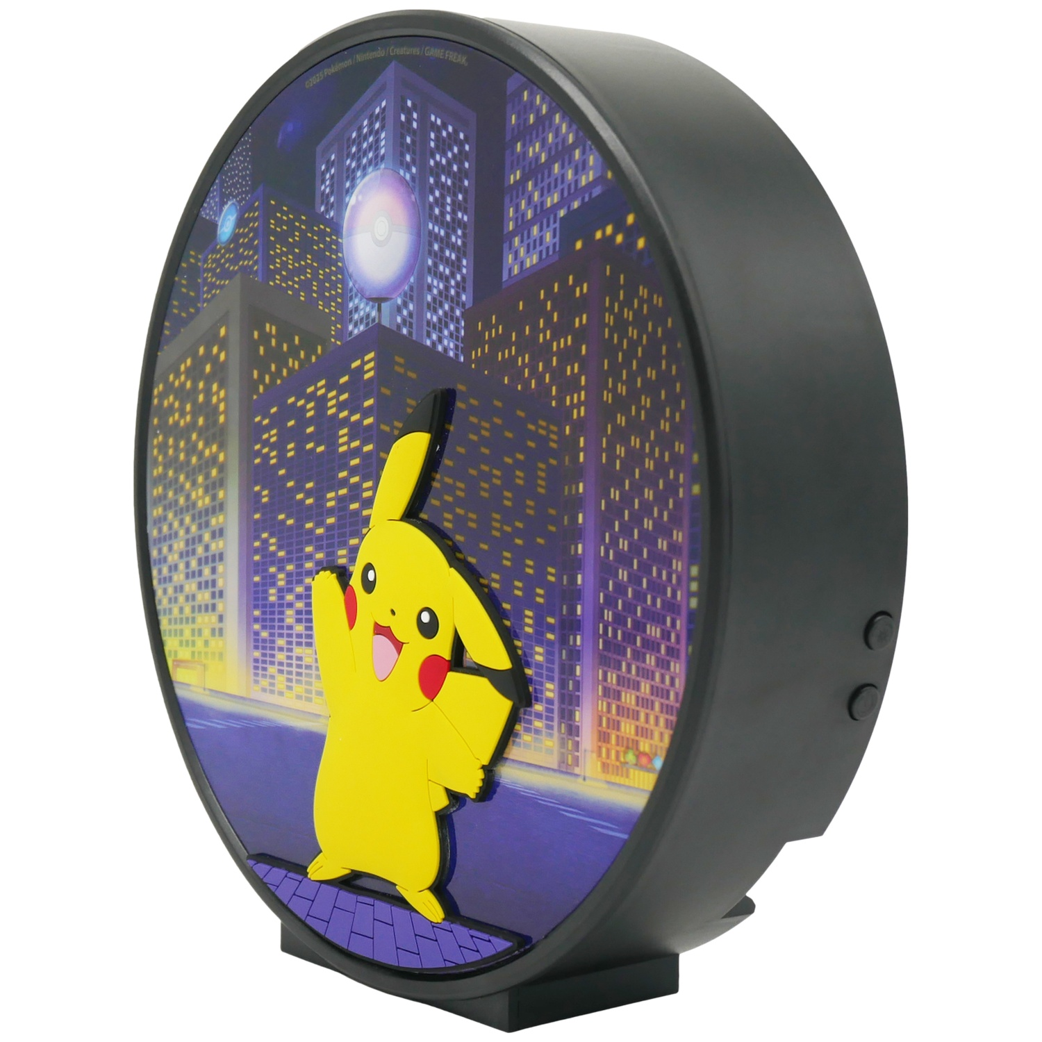 A Pikachu lamp. Yellow Pikachu figure in front of a city scene with tall buildings. Black frame and base.