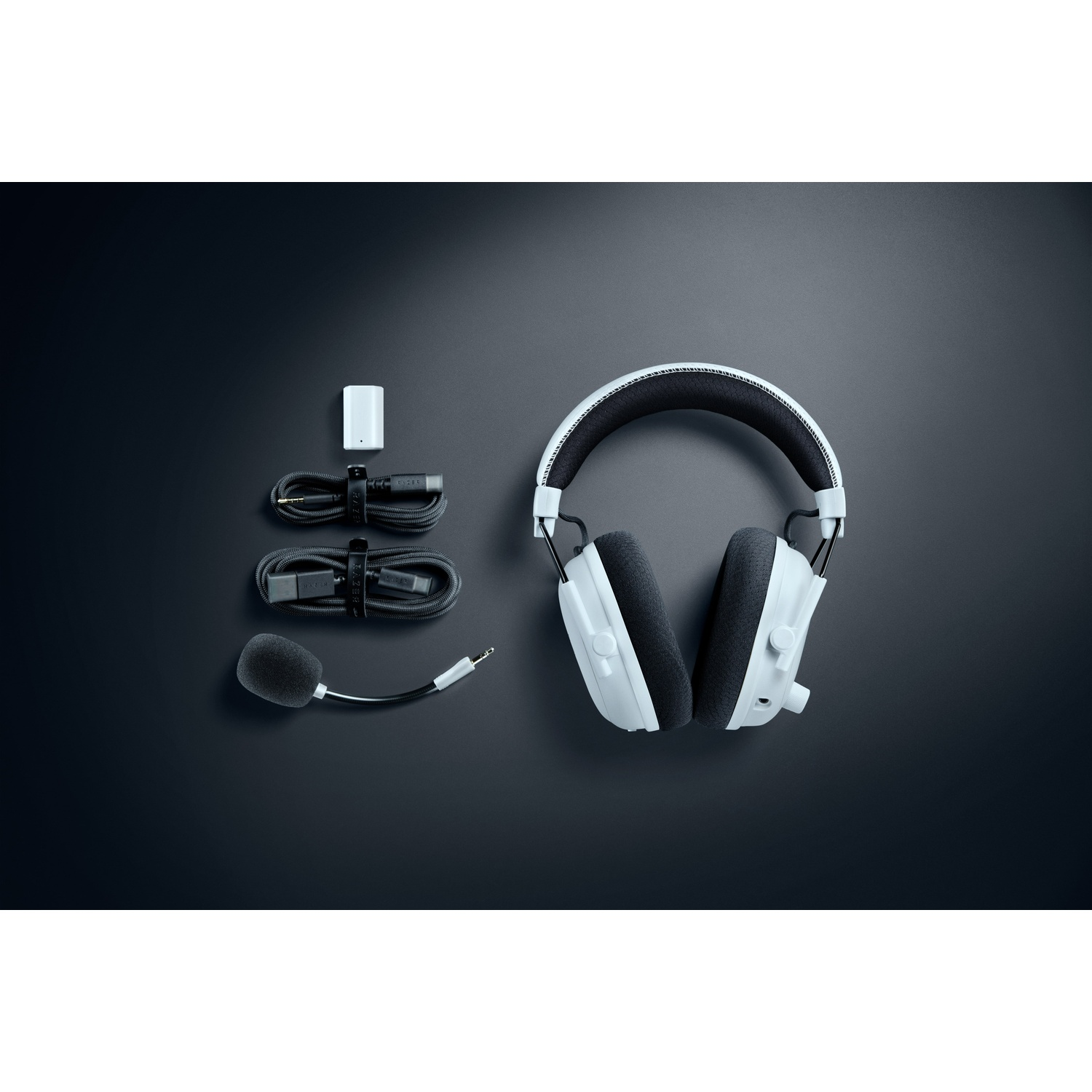 White gaming headset with black earcups, microphone, cables, and a small white receiver on a dark gray surface.